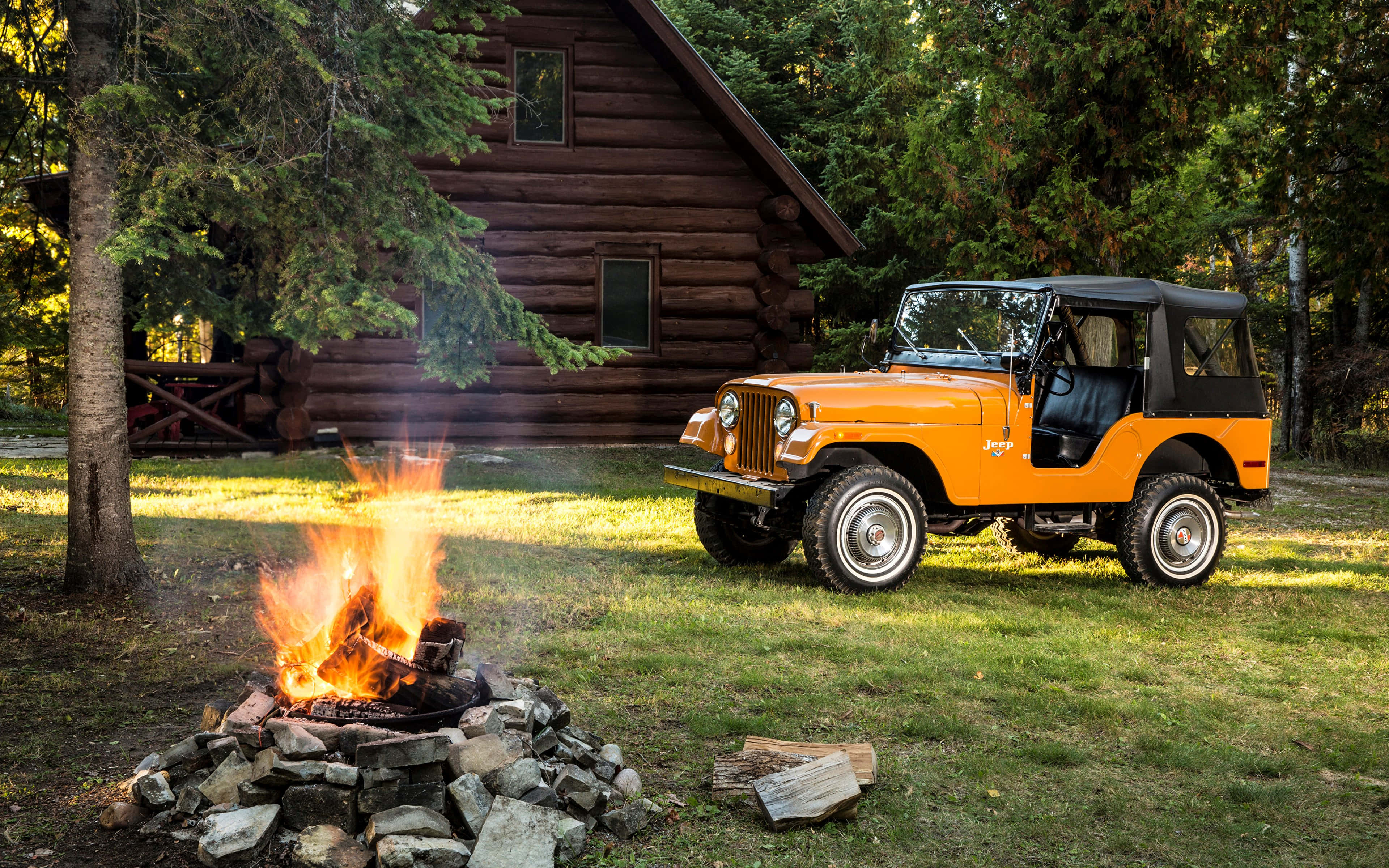 Jeep Cj 桌布 壁紙 — 一輛充滿活力的橙色復古吉普車停在噼啪作響的營火旁，前面是一座被茂密森林環繞的質樸木屋。