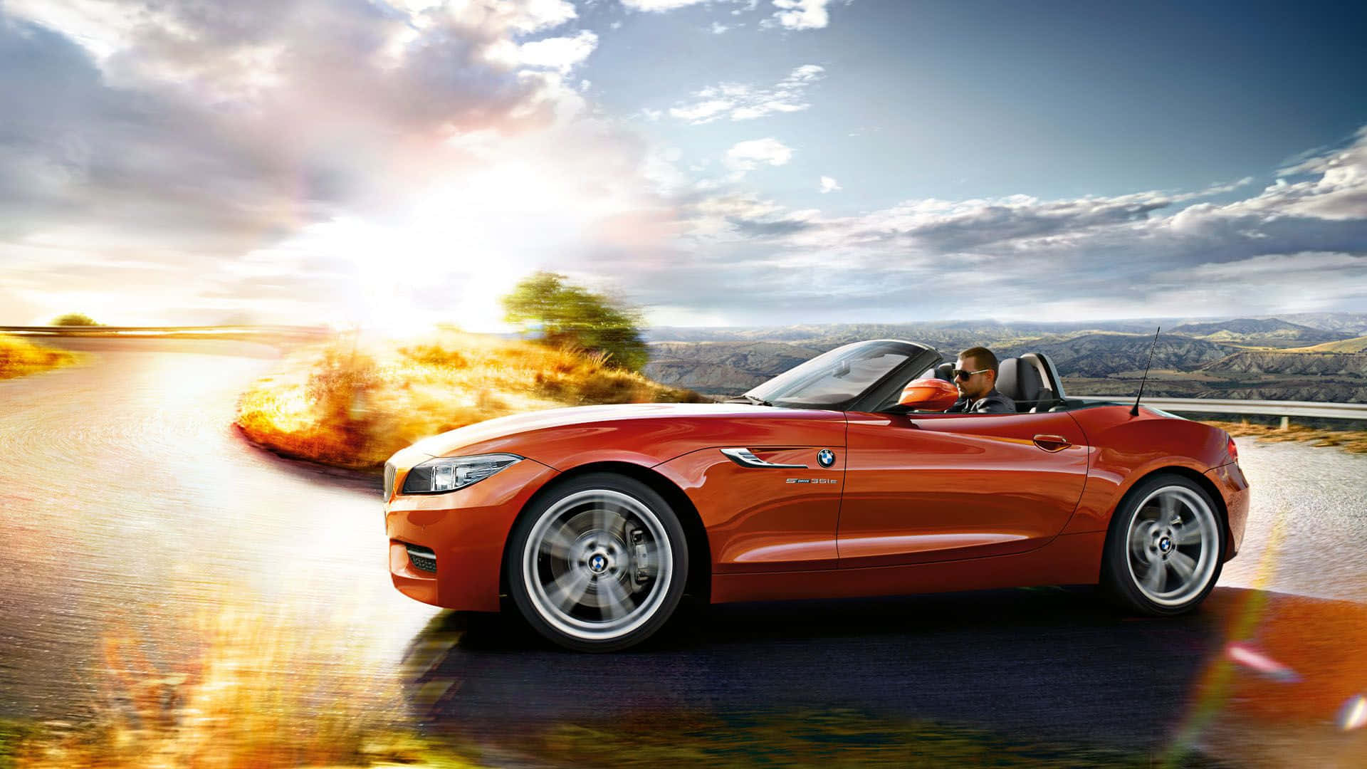 Bmw Z4 桌布 壁紙 — 一輛充滿活力的橙色敞篷跑車在日落時分沿著蜿蜒的道路疾馳，司機享受著露天駕駛的樂趣。