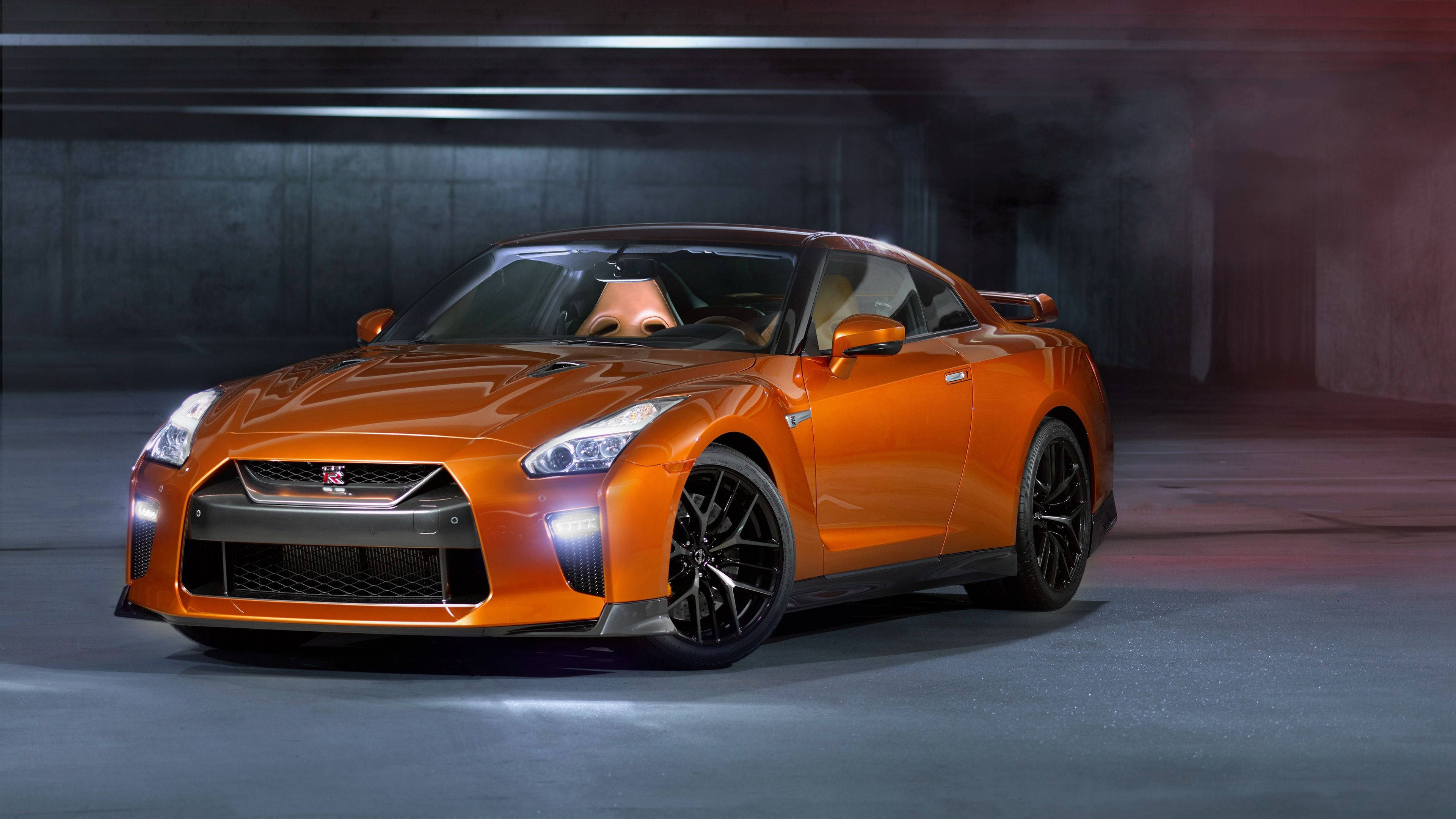 Nissan 桌布 壁紙 — 一輛充滿活力的橙色日產GT-R跑車在煙霧瀰漫的混凝土車庫中，在戲劇性的工作室燈光下閃閃發光。