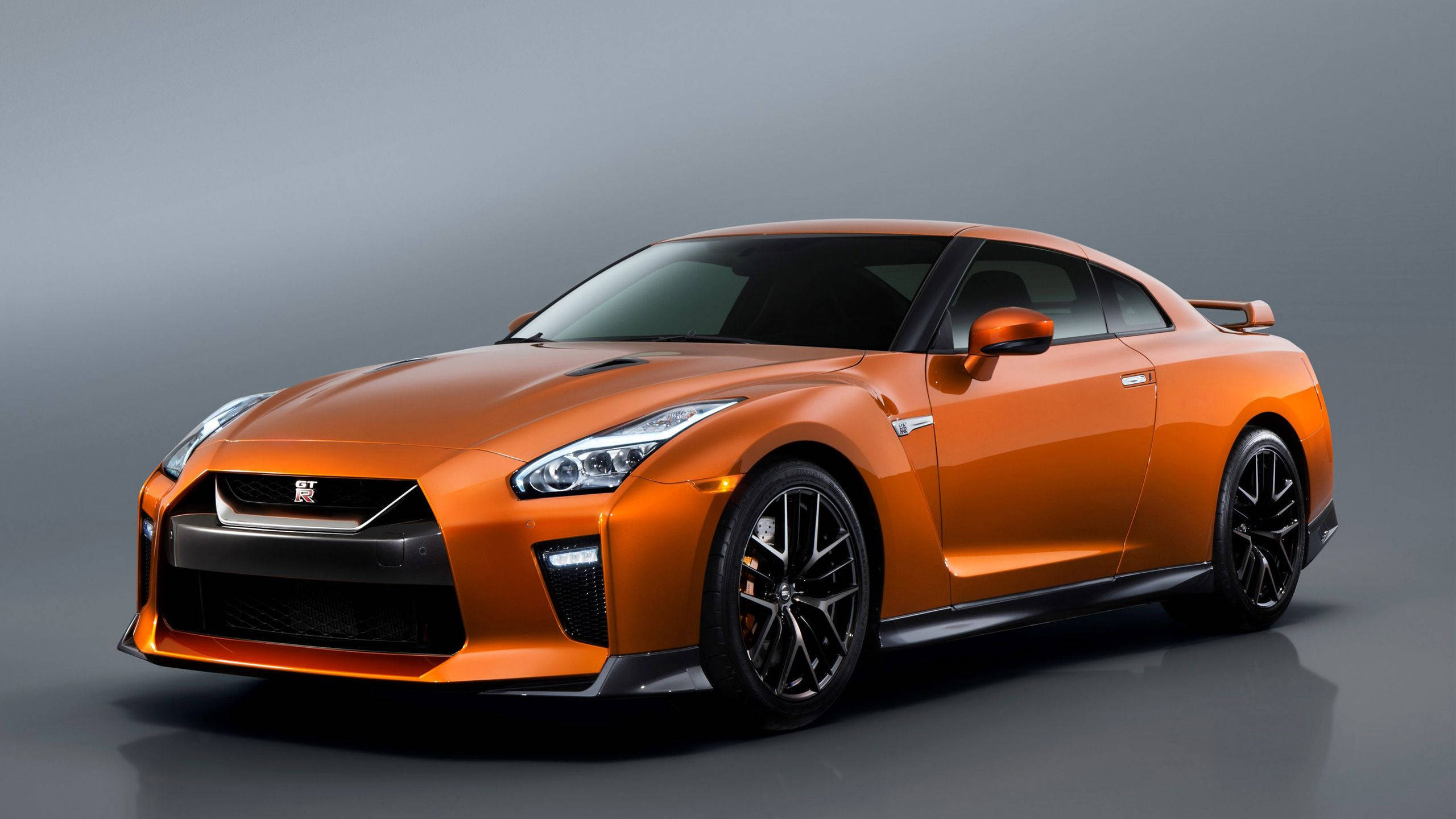 Nissan 桌布 壁紙 — 一輛充滿活力的橙色日產GT-R跑車，帶有黑色點綴和時尚設計，在簡約灰色工作室背景前展示。