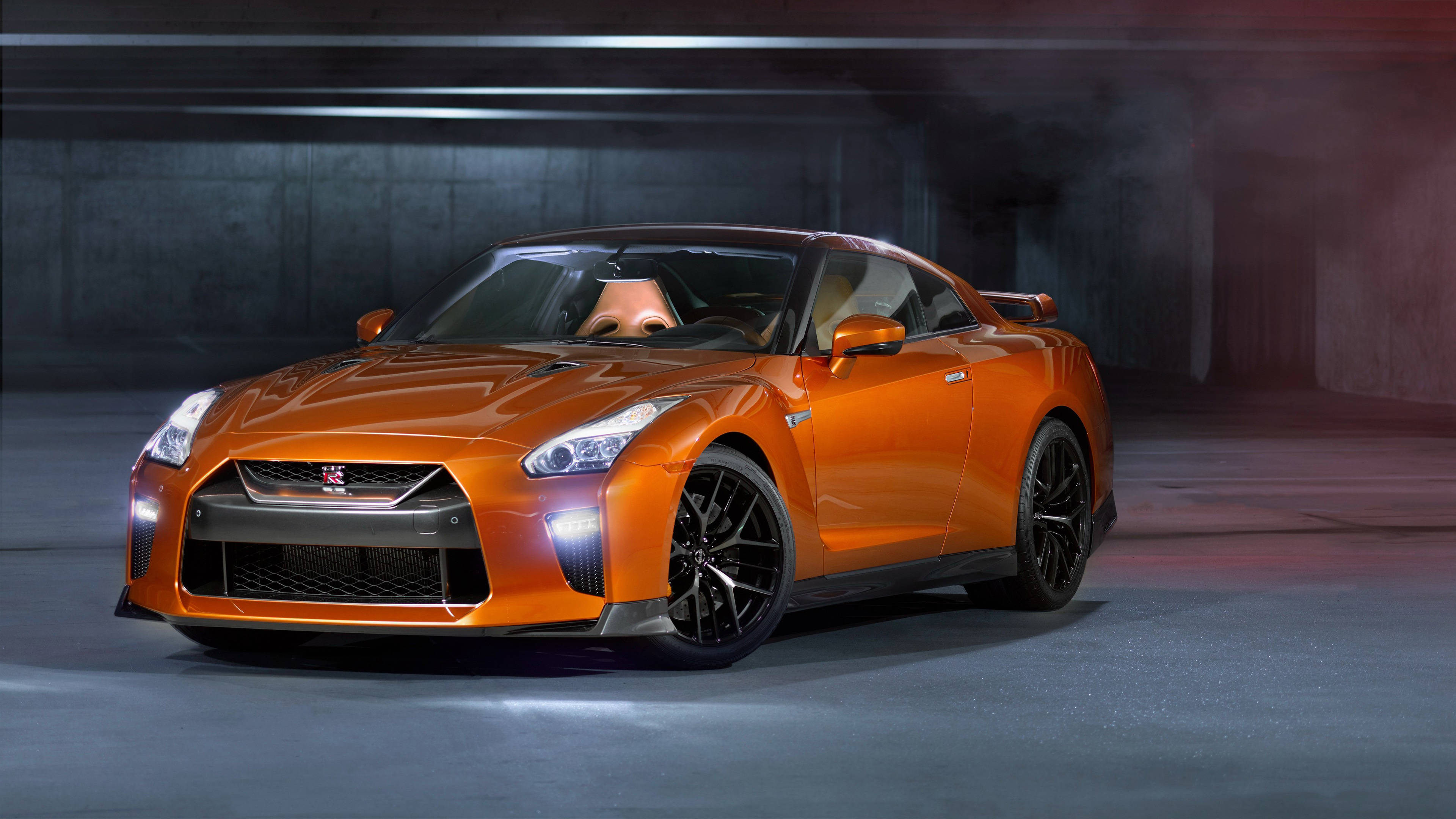 Nissan 桌布 壁紙 — 一輛充滿活力的橙色日產GT-R跑車在煙霧瀰漫的混凝土車庫中，在戲劇性的工作室燈光下閃閃發光。