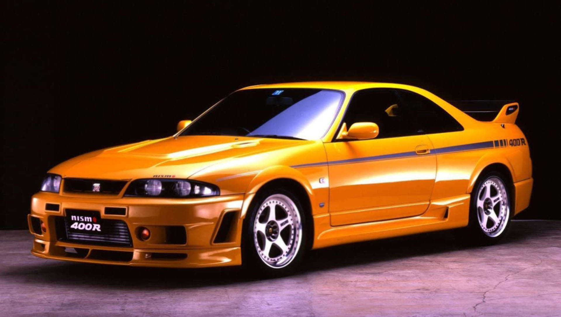 Gtr 桌布 壁紙 — 一輛充滿活力的橙色日產Skyline R34 Nismo 400R跑車在黑色背景下的攝影棚燈光中閃閃發光。