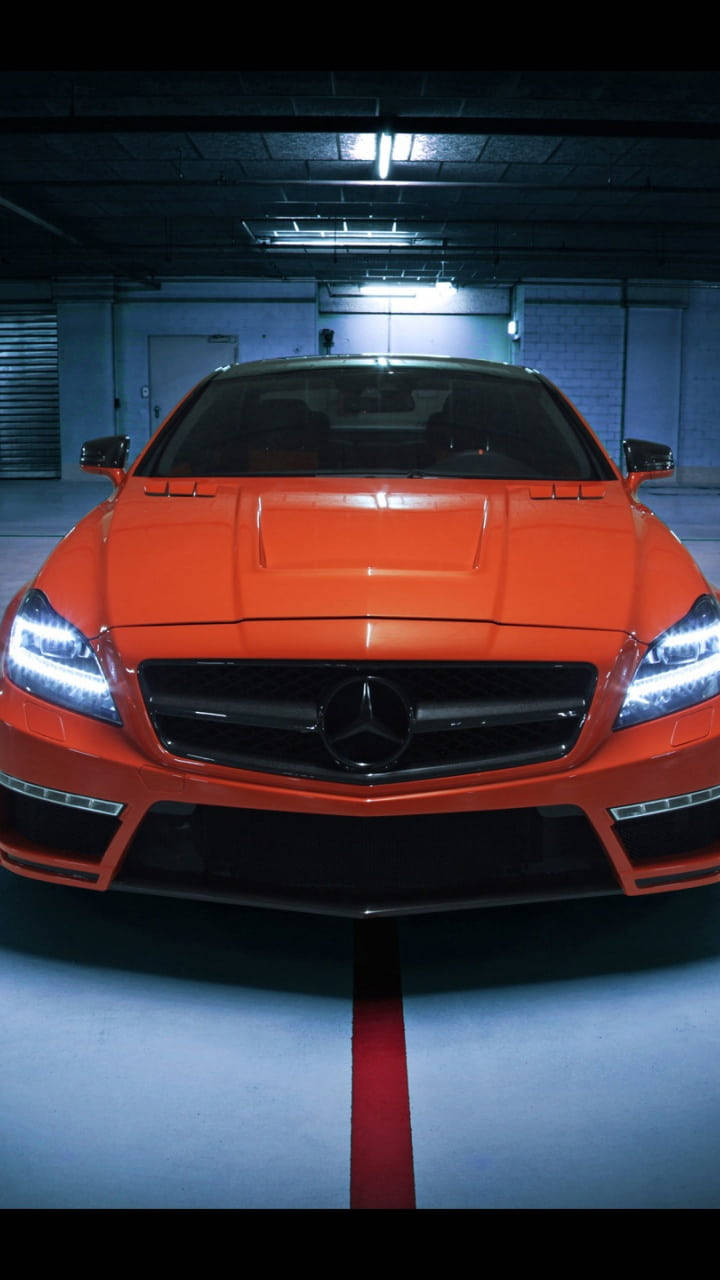 mercedes amg iPhone 桌布 壁紙 — 一輛充滿活力的橙色梅賽德斯跑車在光禿禿的地下停車場的螢光燈下閃閃發光。