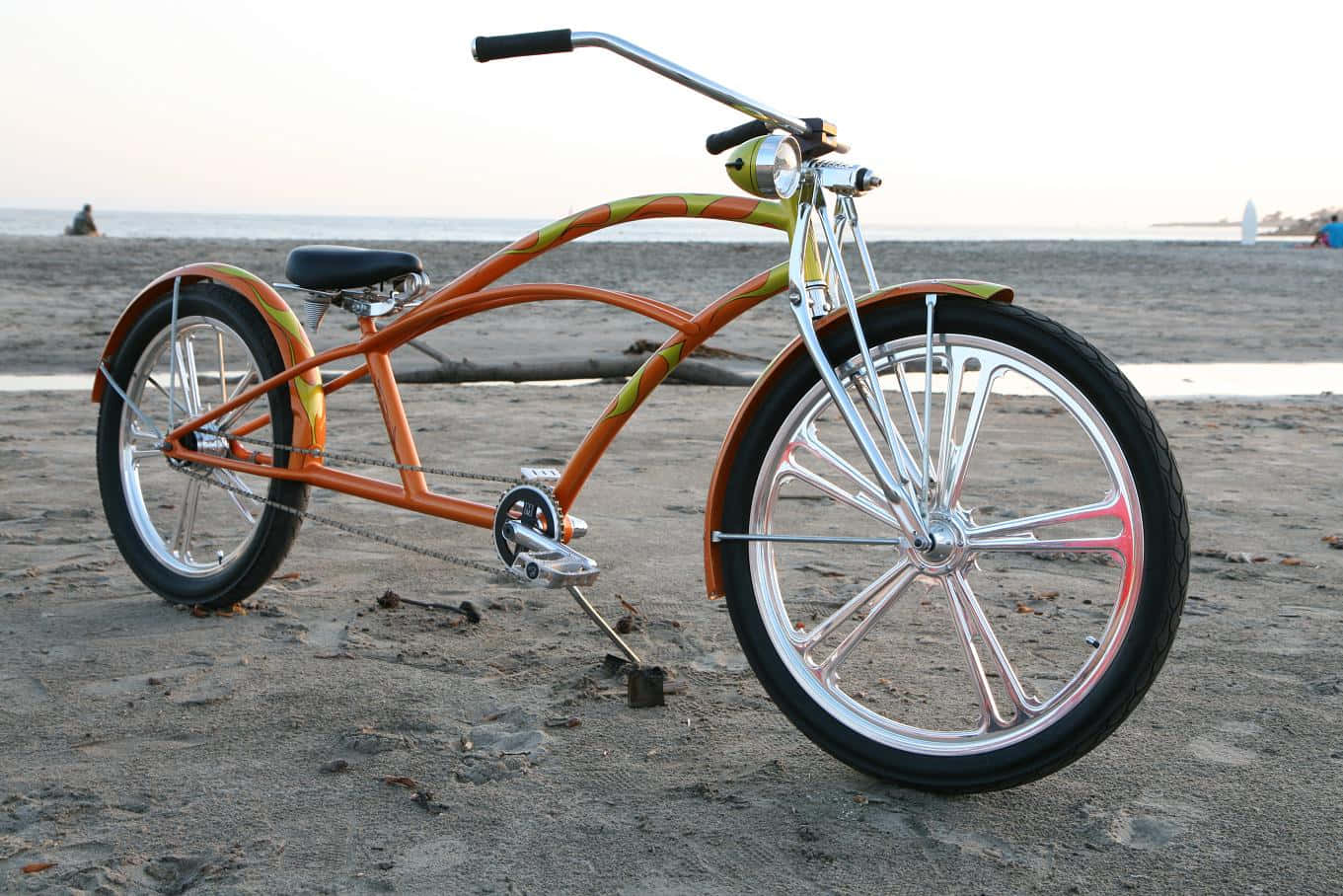 Beach Cruiser 桌布 壁紙 — 一輛充滿活力的橙色沙灘巡航自行車，配備鍍鉻輪圈，在日落時分停放在海邊的濕沙上。