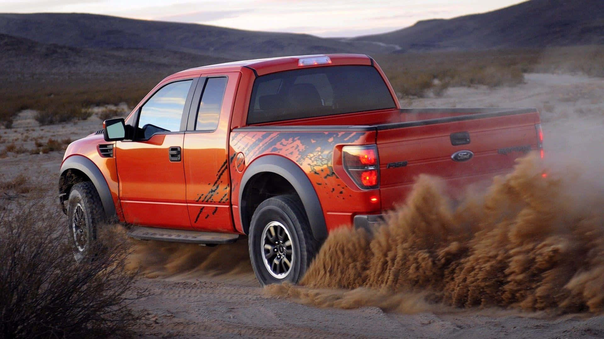 Truck 桌布 壁紙 — 一輛充滿活力的橙色福特 F-150 Raptor 在塵土飛揚的沙漠景觀中飛馳，揚起巨大的沙塵雲。