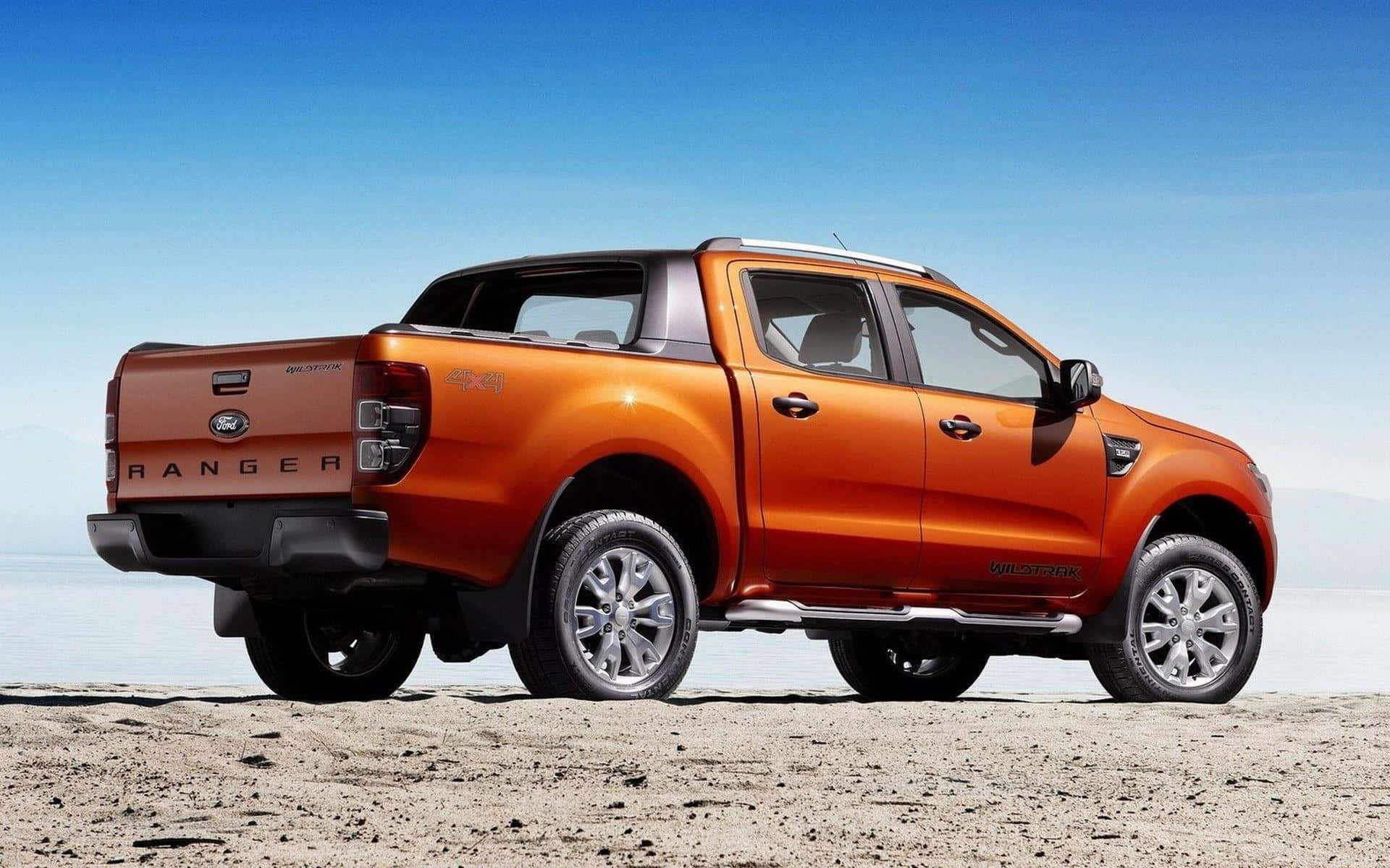 Ford Ranger 桌布 壁紙 — 一輛充滿活力的橙色福特 Ranger 皮卡車停放在陽光明媚的沙漠景觀中，天空湛藍清澈。