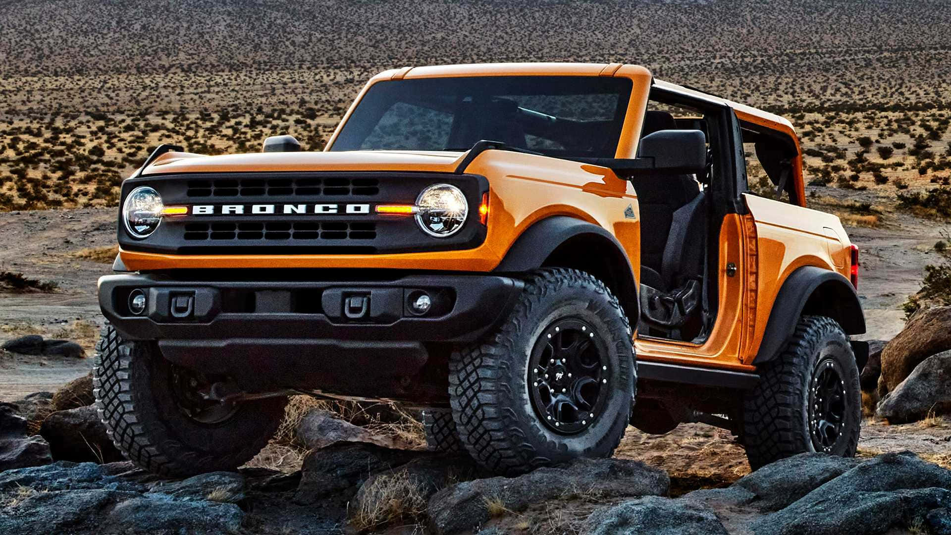 Ford Bronco 桌布 壁紙 — 一輛充滿活力的橙色福特Bronco敞開車門，在晴朗的天空下傲然矗立在岩石沙漠地形上。