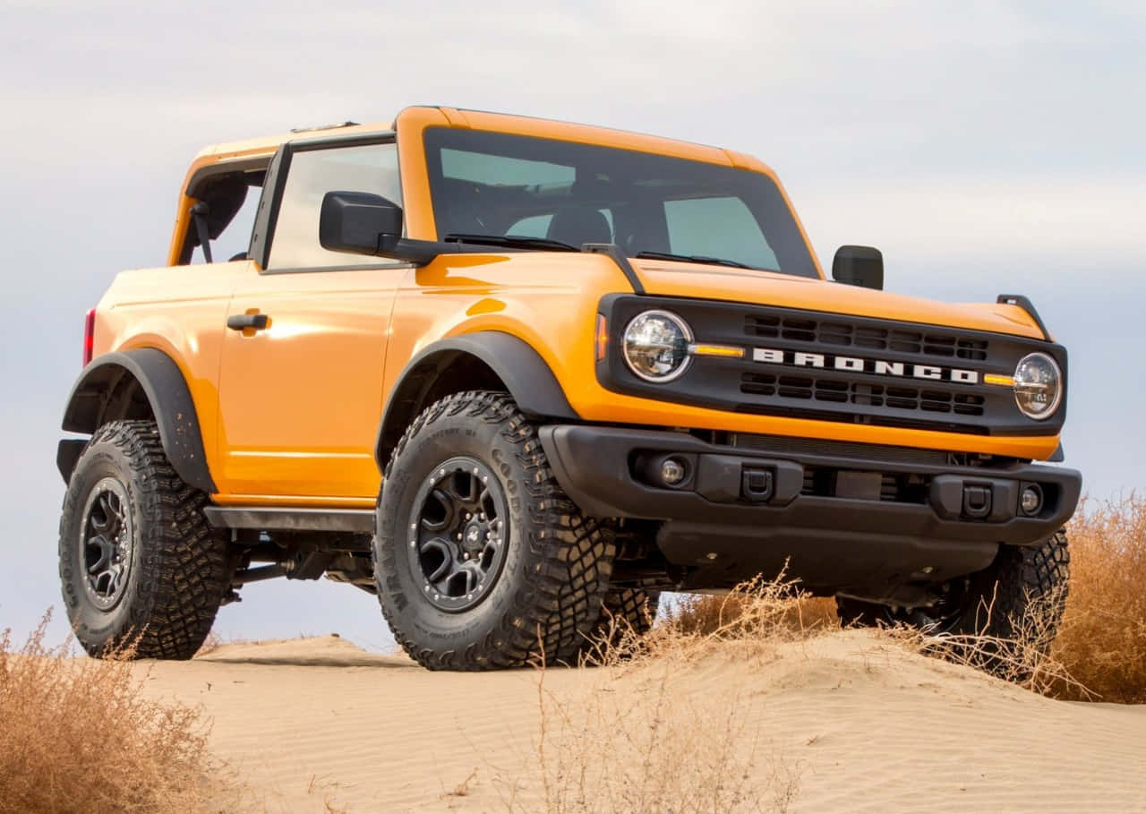 福特野馬越野車 桌布 壁紙 — 一輛充滿活力的橙色福特Bronco SUV停泊在沙丘上，周圍有乾草，天空蒼白。