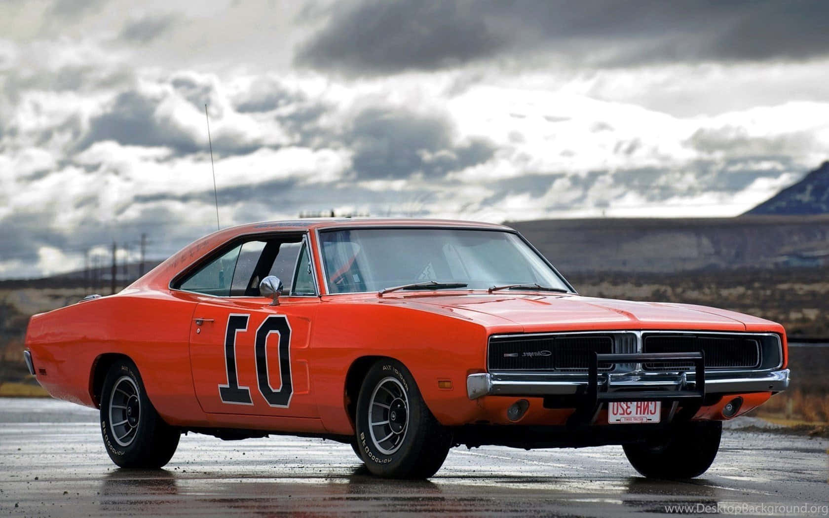 General Lee 車 桌布 壁紙 — 一輛充滿活力的橙色經典肌肉車，帶有黑色賽車貼紙號碼10，停在潮濕的道路上，天空戲劇性地多雲。