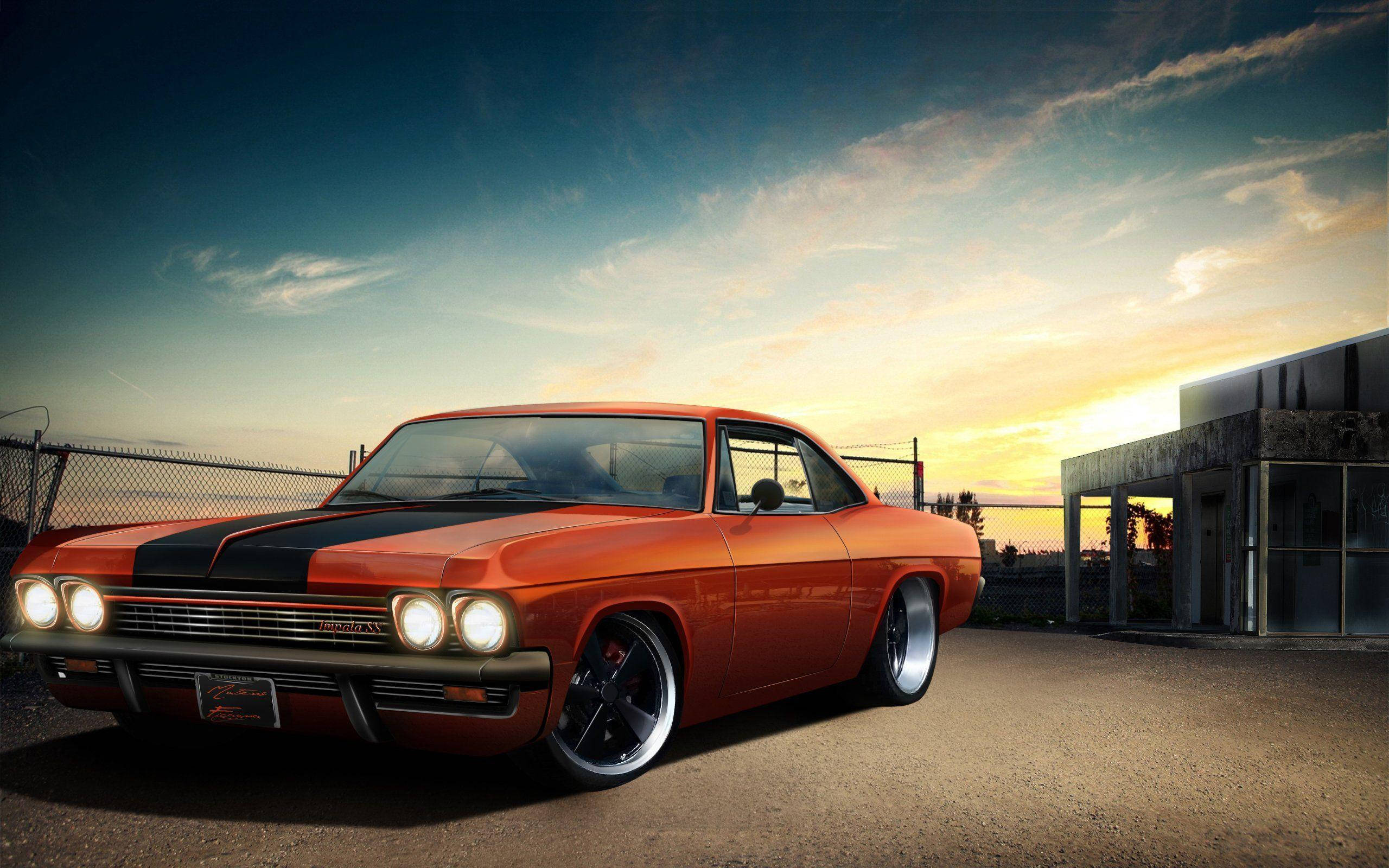 chevrolet impala 1967 桌布 壁紙 — 一輛充滿活力的橙色經典肌肉車帶有黑色條紋，在夕陽天空下閃閃發光，旁邊是鐵絲網圍欄和混凝土建築。
