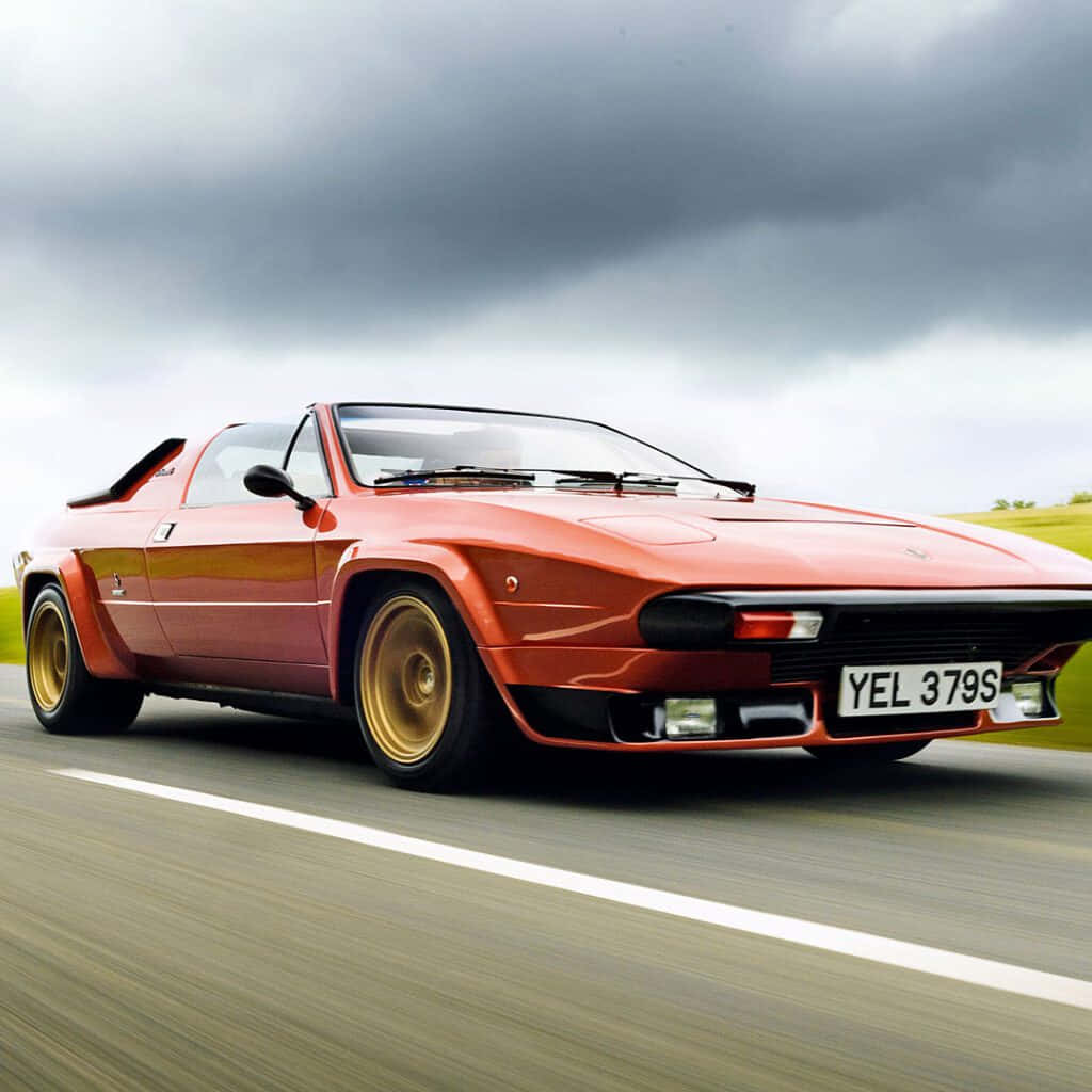 Lamborghini Silhouette 桌布 壁紙 — 一輛充滿活力的橙色經典跑車在戲劇性的多雲天空下行駛在道路上。