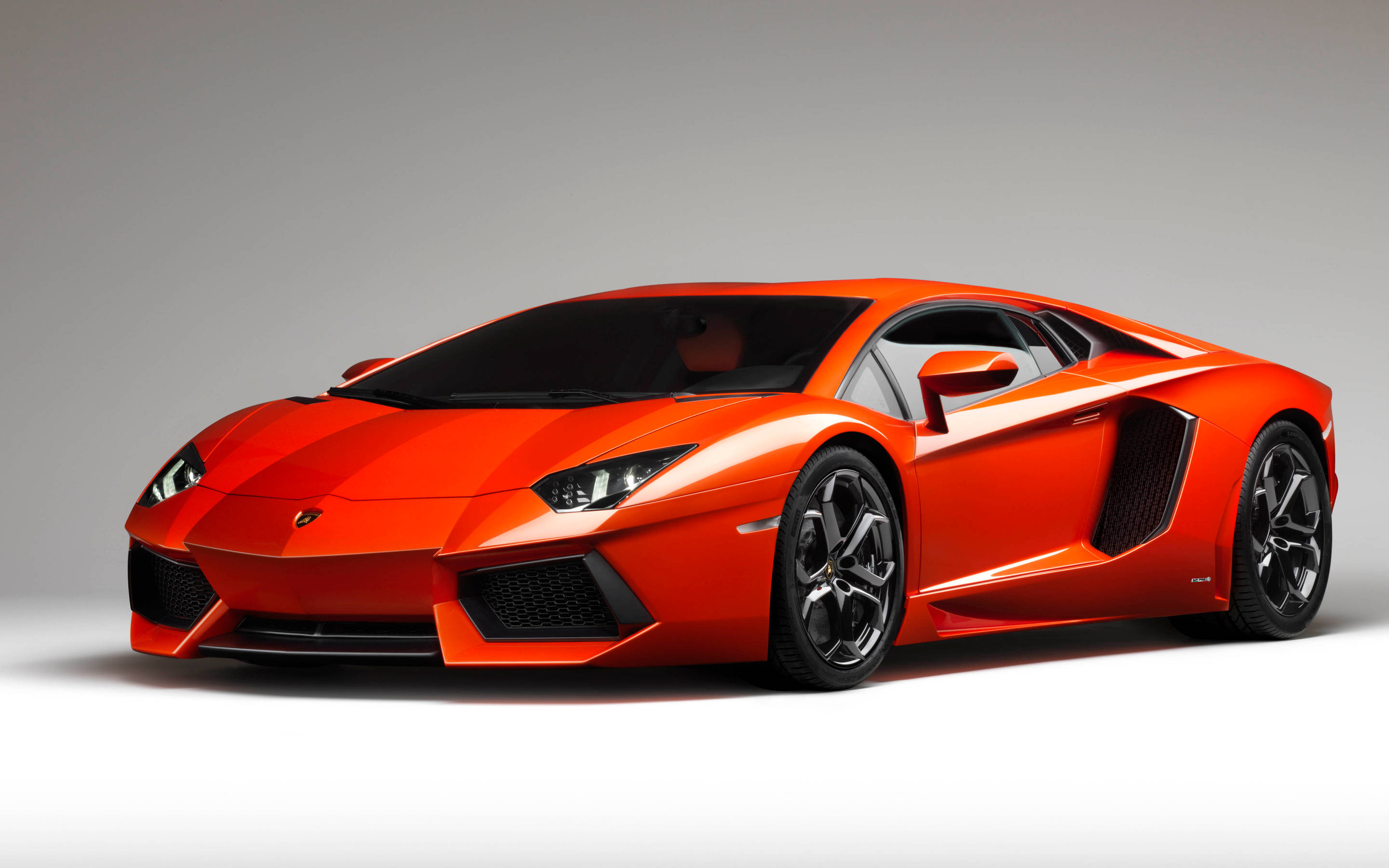 4K 藍寶堅尼 桌布 壁紙 — 一輛充滿活力的橙色藍寶堅尼Aventador跑車，帶有黑色飾邊和流線型空氣動力學設計，在極簡灰色工作室背景下擺拍。