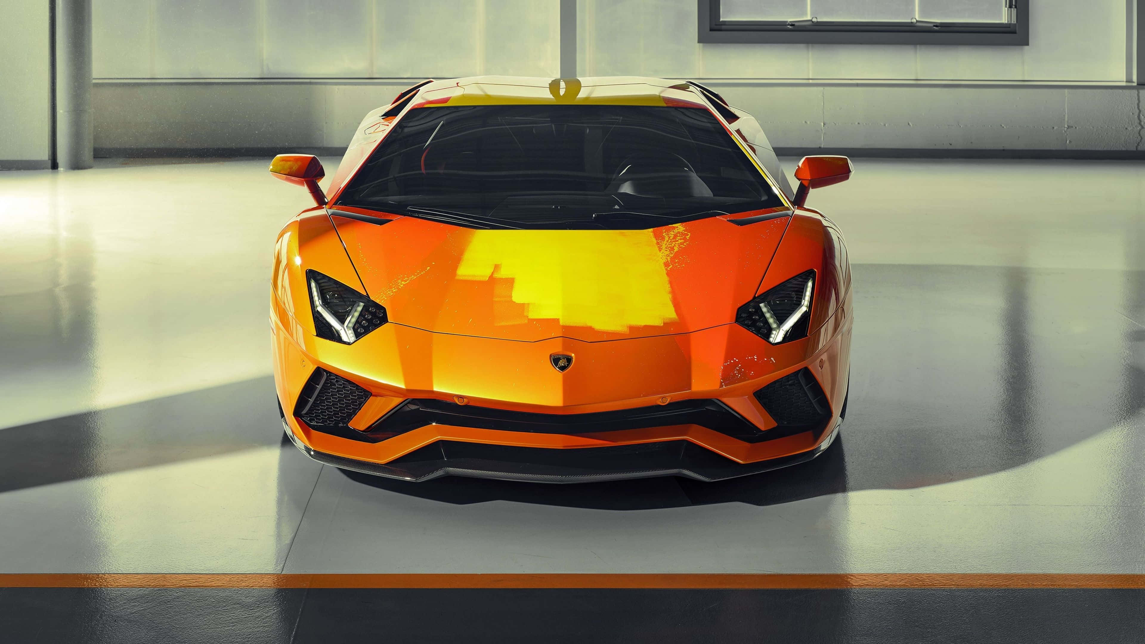 4K 藍寶堅尼 桌布 壁紙 — 一輛充滿活力的橙色藍寶堅尼Aventador，帶有像素化黃色點綴，在簡約車庫中正面朝前，處於明亮的攝影棚燈光下。