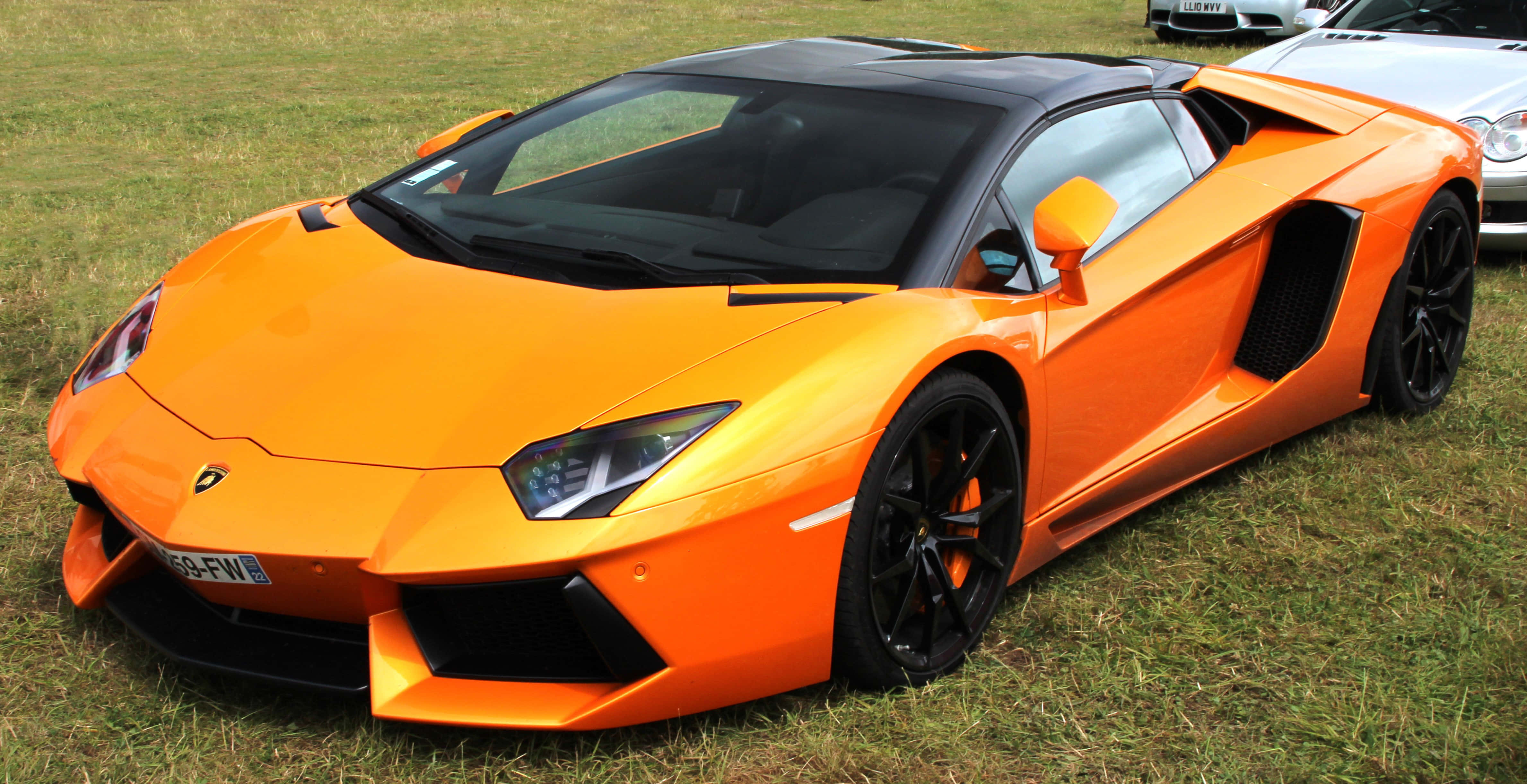 Lamborghini Aventador 桌布 壁紙 — 一輛充滿活力的橙色藍寶堅尼Aventador跑車停放在草地上，帶有黑色飾邊和流線型空氣動力學設計。