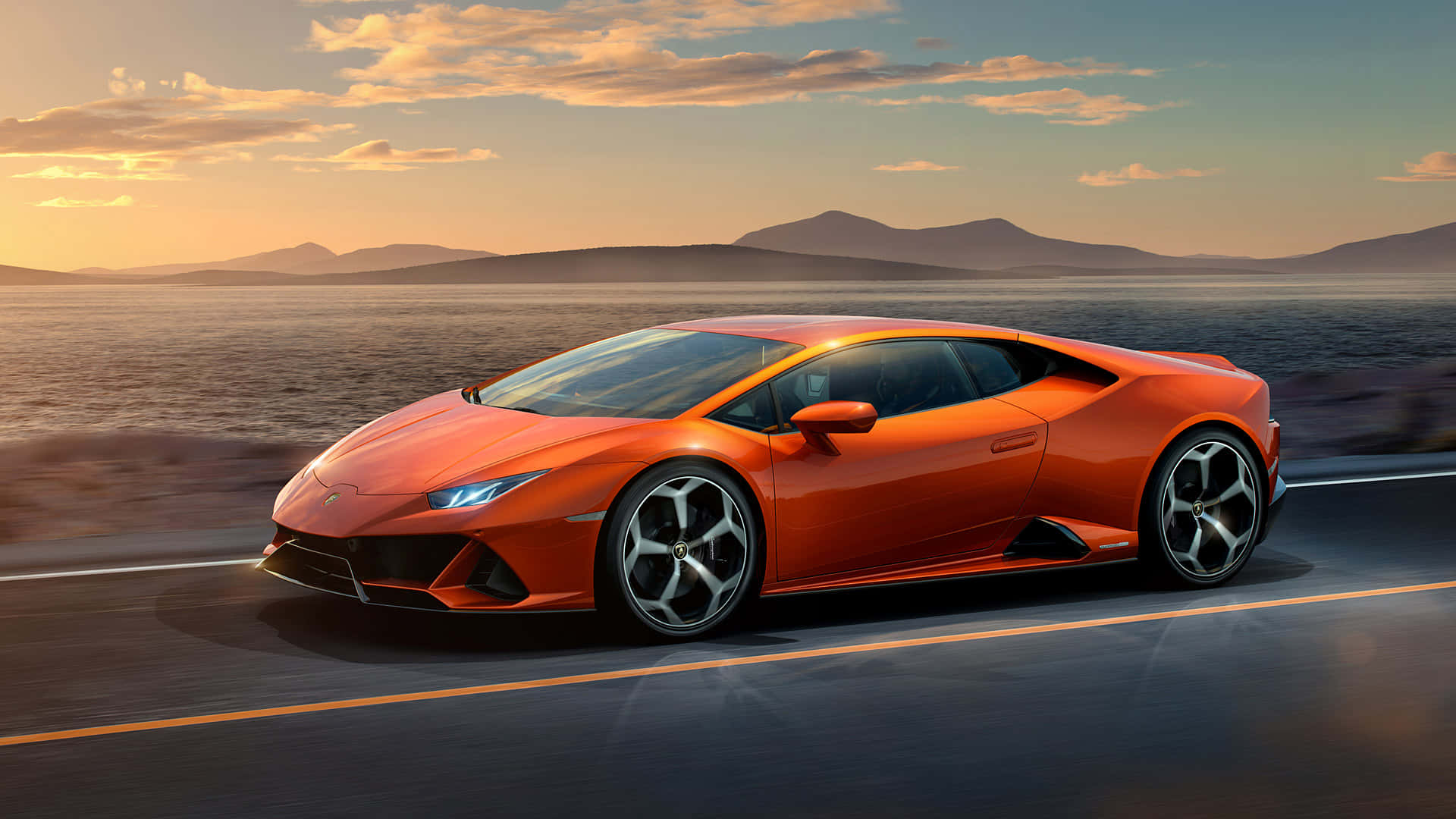 Cool Car 桌布 壁紙 — 一輛充滿活力的橙色藍寶堅尼Huracán在日落時分沿著沙漠高速公路疾駛，遠處有山巒。