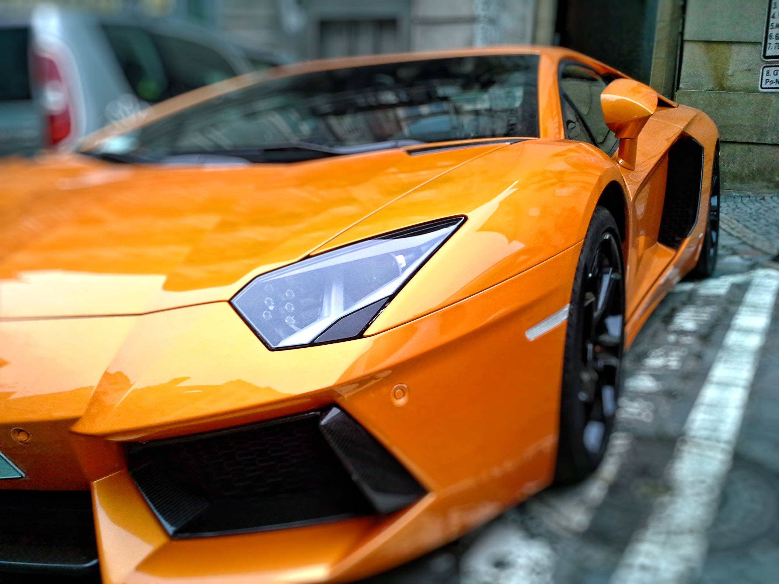 Metallic 桌布 壁紙 — 一輛充滿活力的橙色藍寶堅尼跑車停泊在濕漉漉的城市街道上，帶有倒影和城市背景。