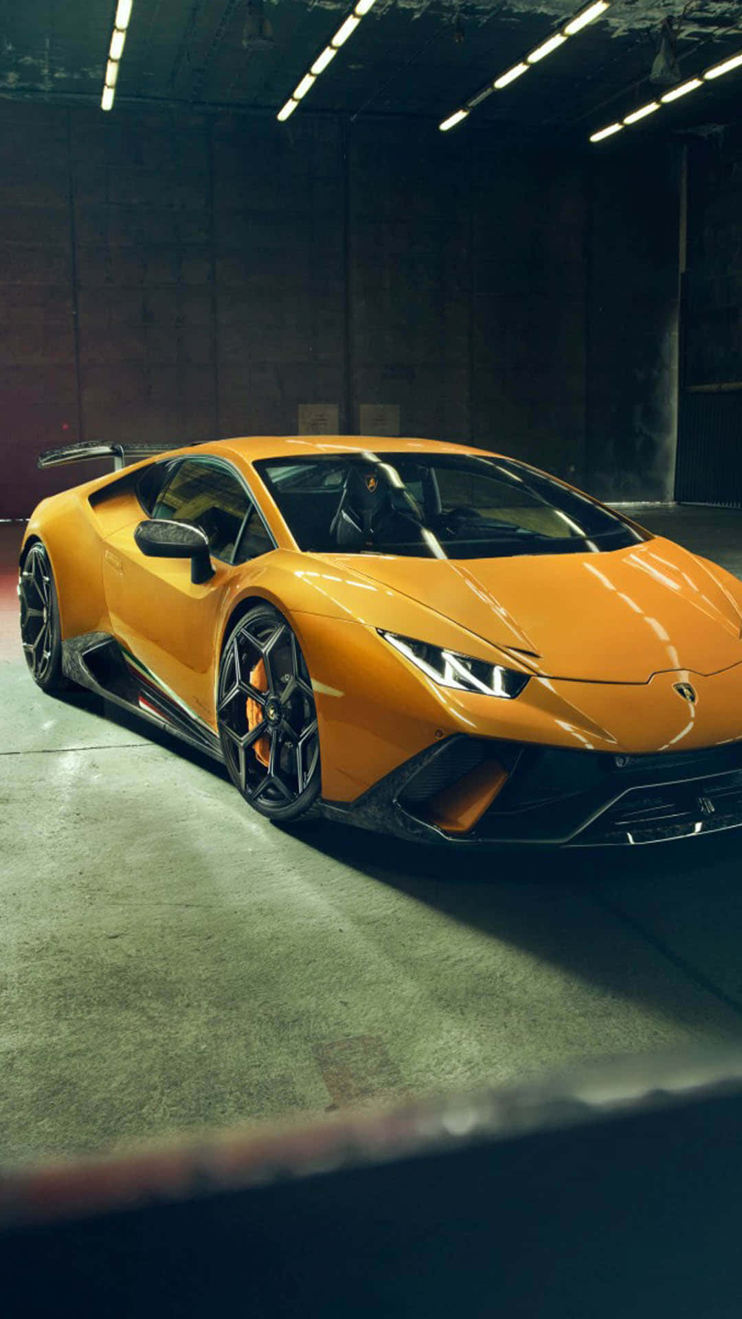 Pixel 3xl Lamborghini 桌布 壁紙 — 一輛充滿活力的橙色藍寶堅尼跑車在昏暗的混凝土車庫中，在工業燈光下閃閃發光。
