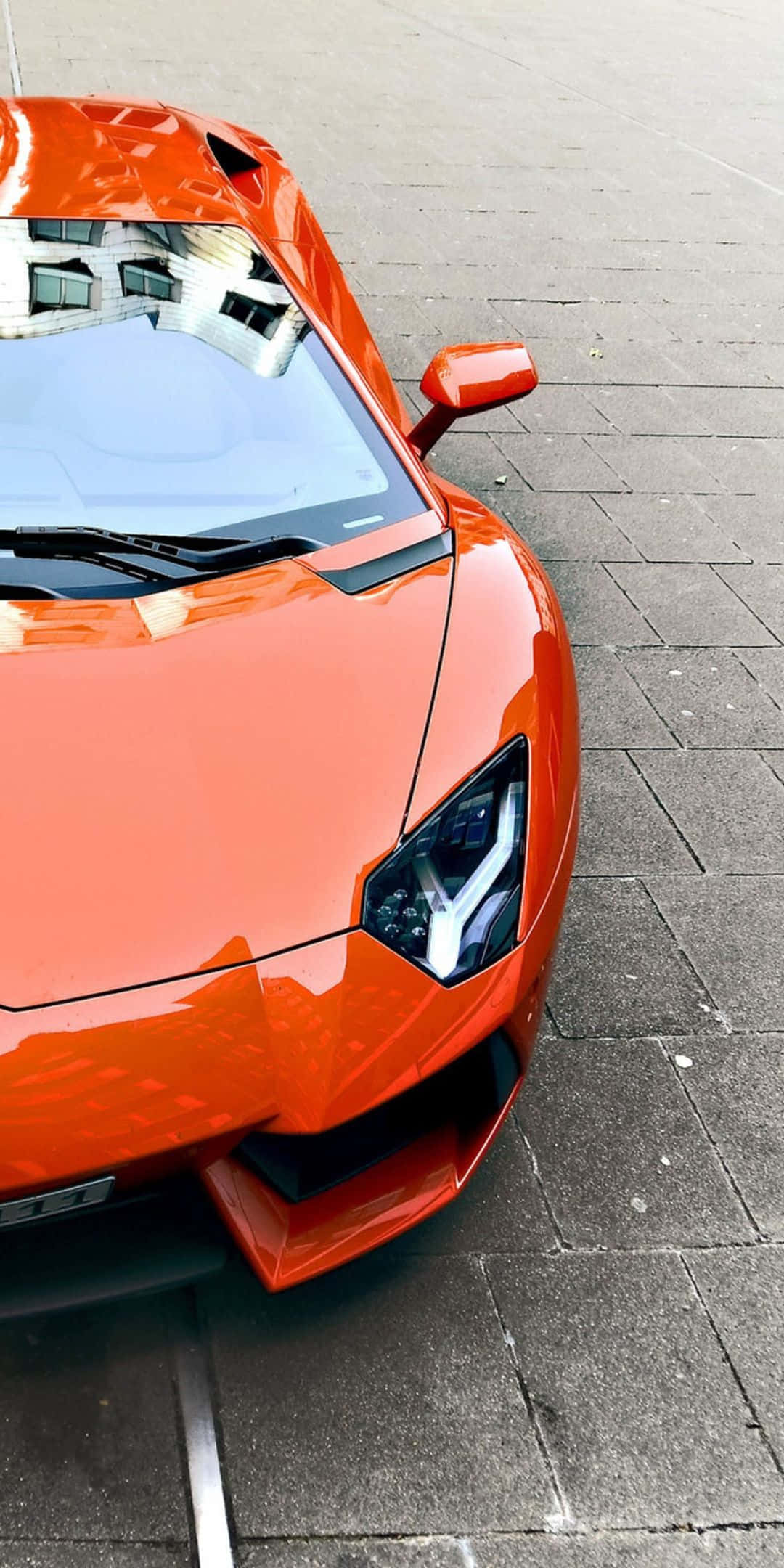 Pixel 3 Lamborghini 桌布 壁紙 — 一輛充滿活力的橙色藍寶堅尼跑車在明亮的日光下在灰色石鋪路面上閃閃發光。