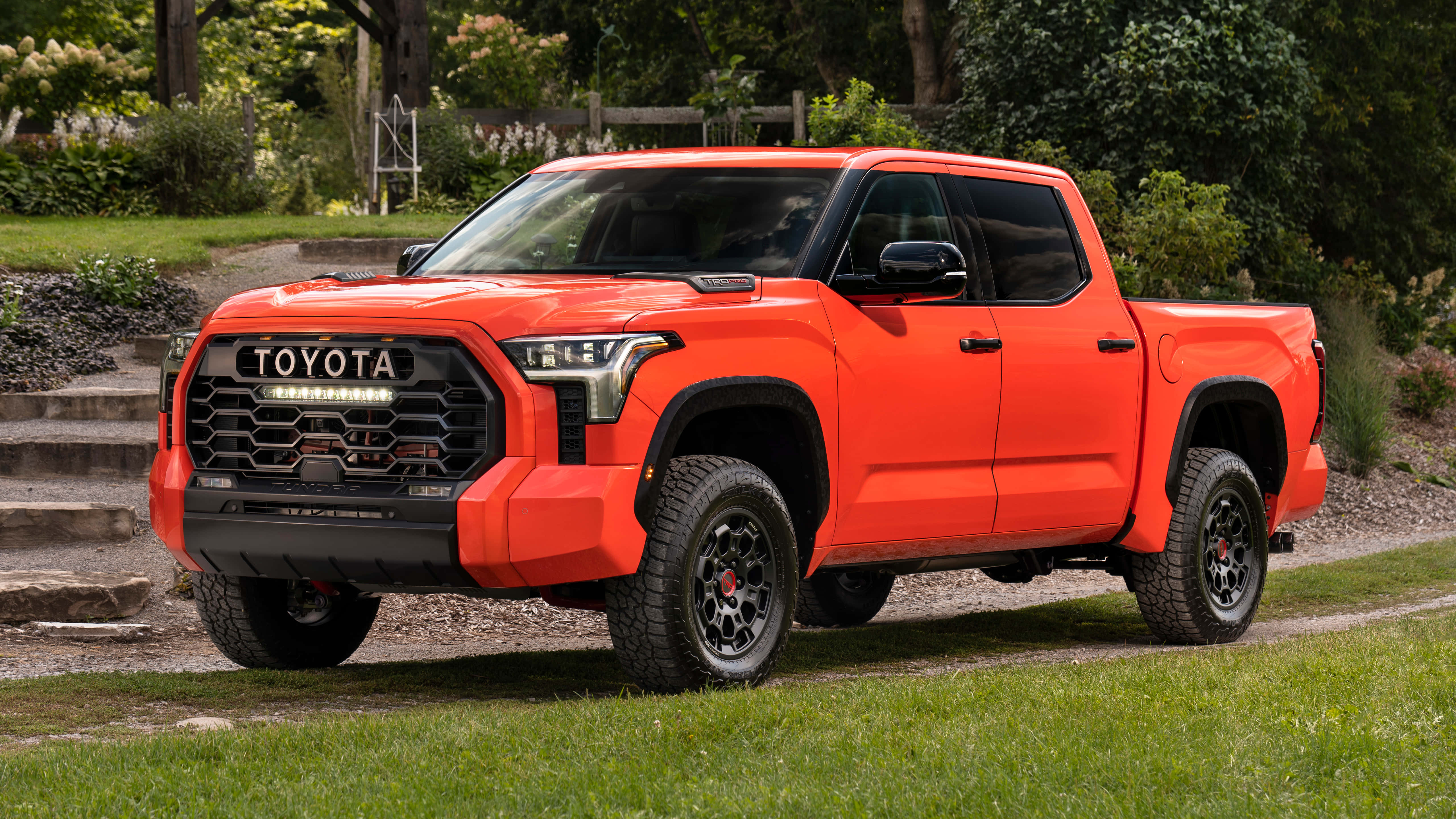 Toyota 桌布 壁紙 — 一輛充滿活力的橙色豐田Tacoma pickup truck停放在石階旁邊的草地上，背景是茂密的綠植。