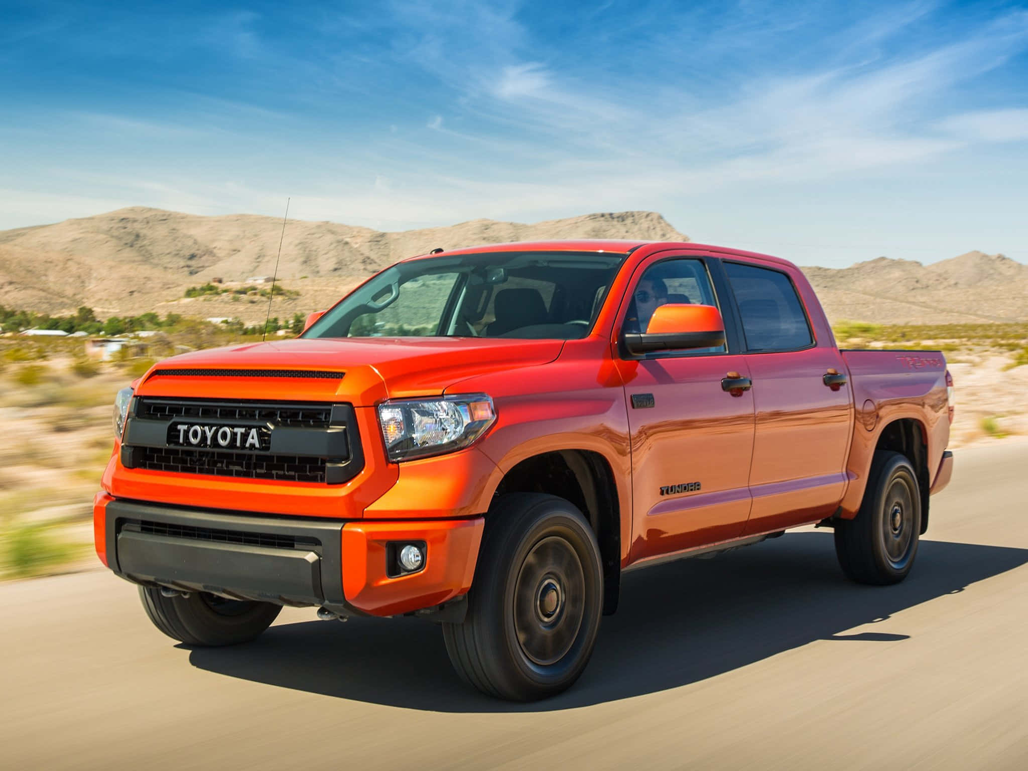Toyota 桌布 壁紙 — 一輛充滿活力的橙色豐田Tundra pickup truck在沙漠公路上高速行駛，背景是乾燥的山丘和清澈的藍天，呈現動態模糊效果。