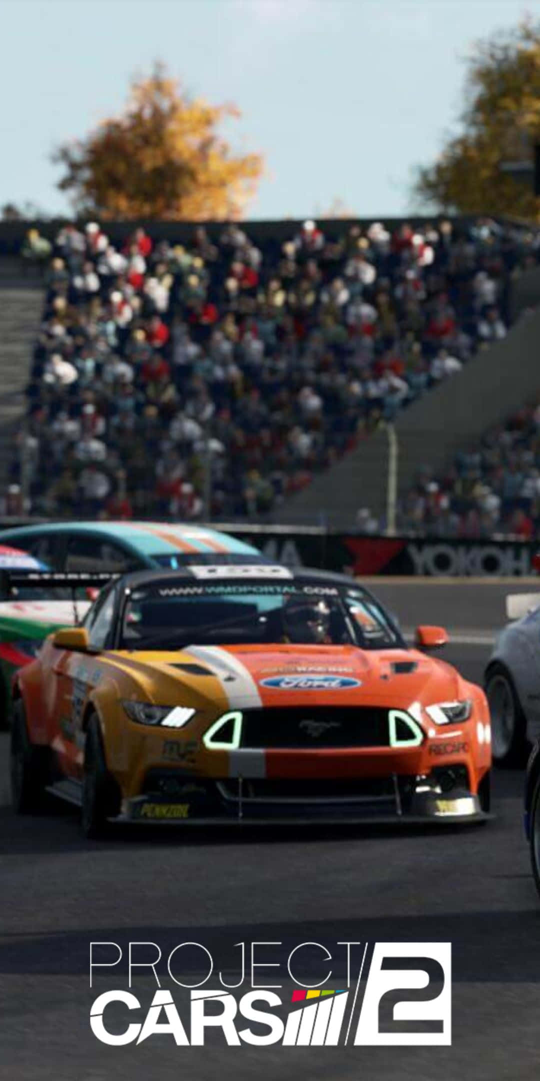 Pixel 3 Project Cars 2 桌布 壁紙 — 一輛充滿活力的橙色賽車在晴朗的天空下，在賽道上飛馳，看台上觀眾模糊不清。