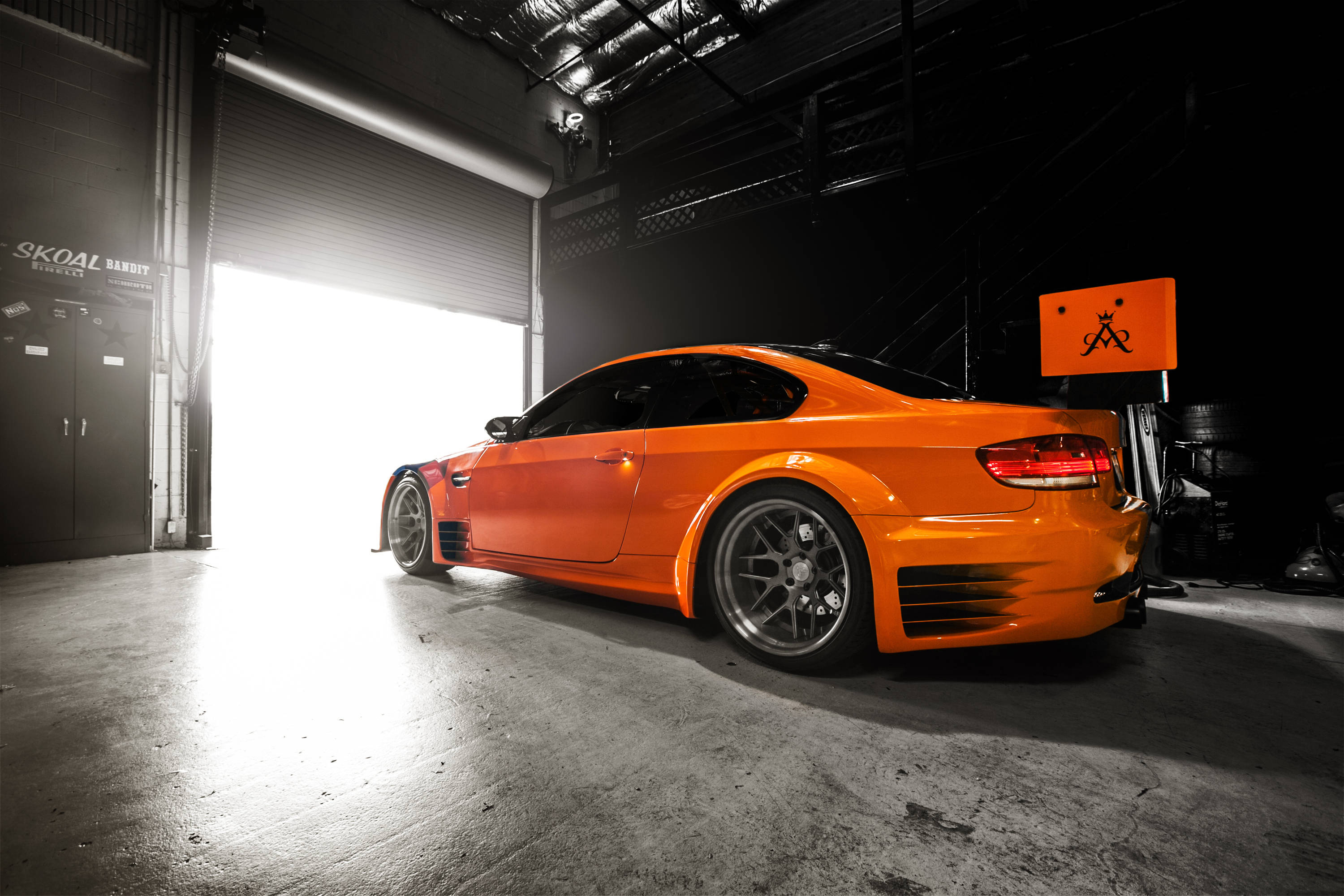 Bmw M Series 桌布 壁紙 — 一輛充滿活力的橙色跑車在昏暗的工業車庫內，在戲劇性的背光下閃閃發光。