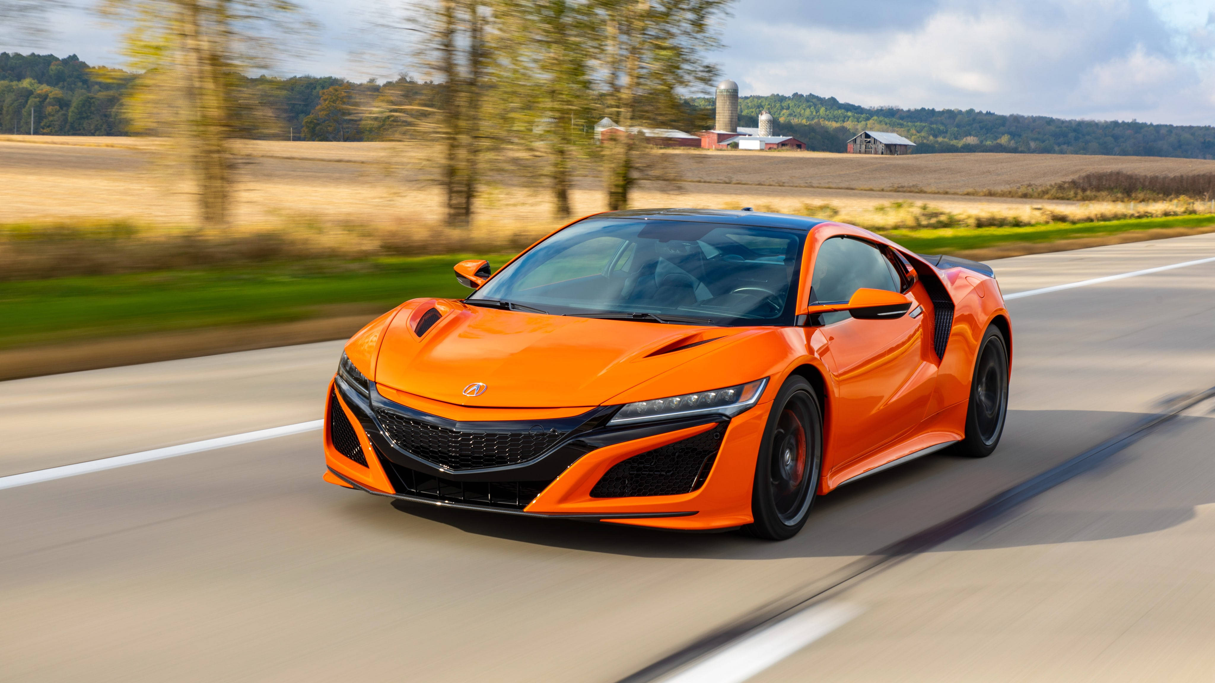 Acura 桌布 壁紙 — 一輛充滿活力的橙色跑車在鄉村道路上飛馳，背景是模糊的樹木和農場建築。