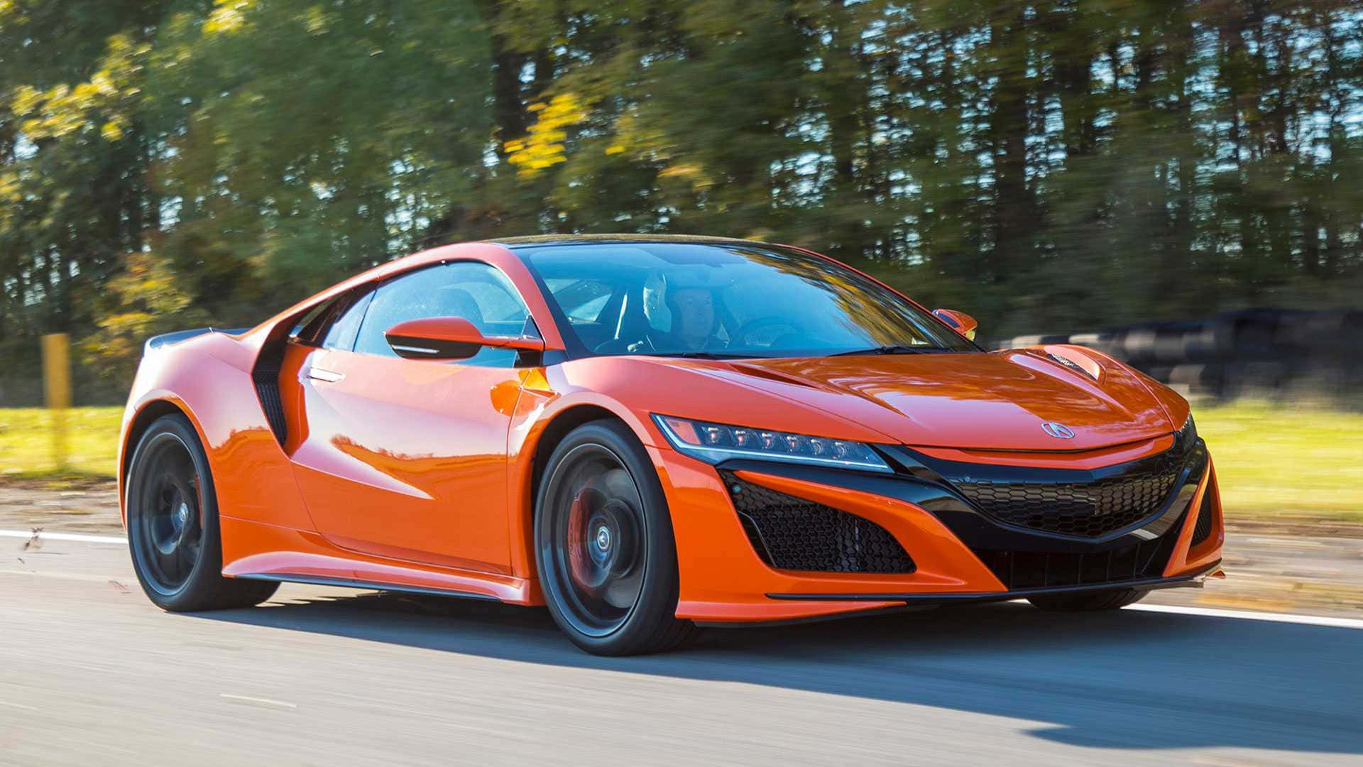 Acura 桌布 壁紙 — 一輛充滿活力的橙色跑車在陽光明媚的道路上行駛，背景是模糊的綠色樹木。