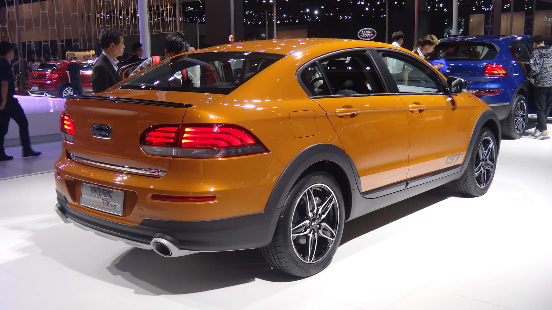 Qoros 桌布 壁紙 — 一輛充滿活力的橙色跨界SUV，配備時尚尾燈和黑色飾邊，在車展上展出，人們正在觀看。