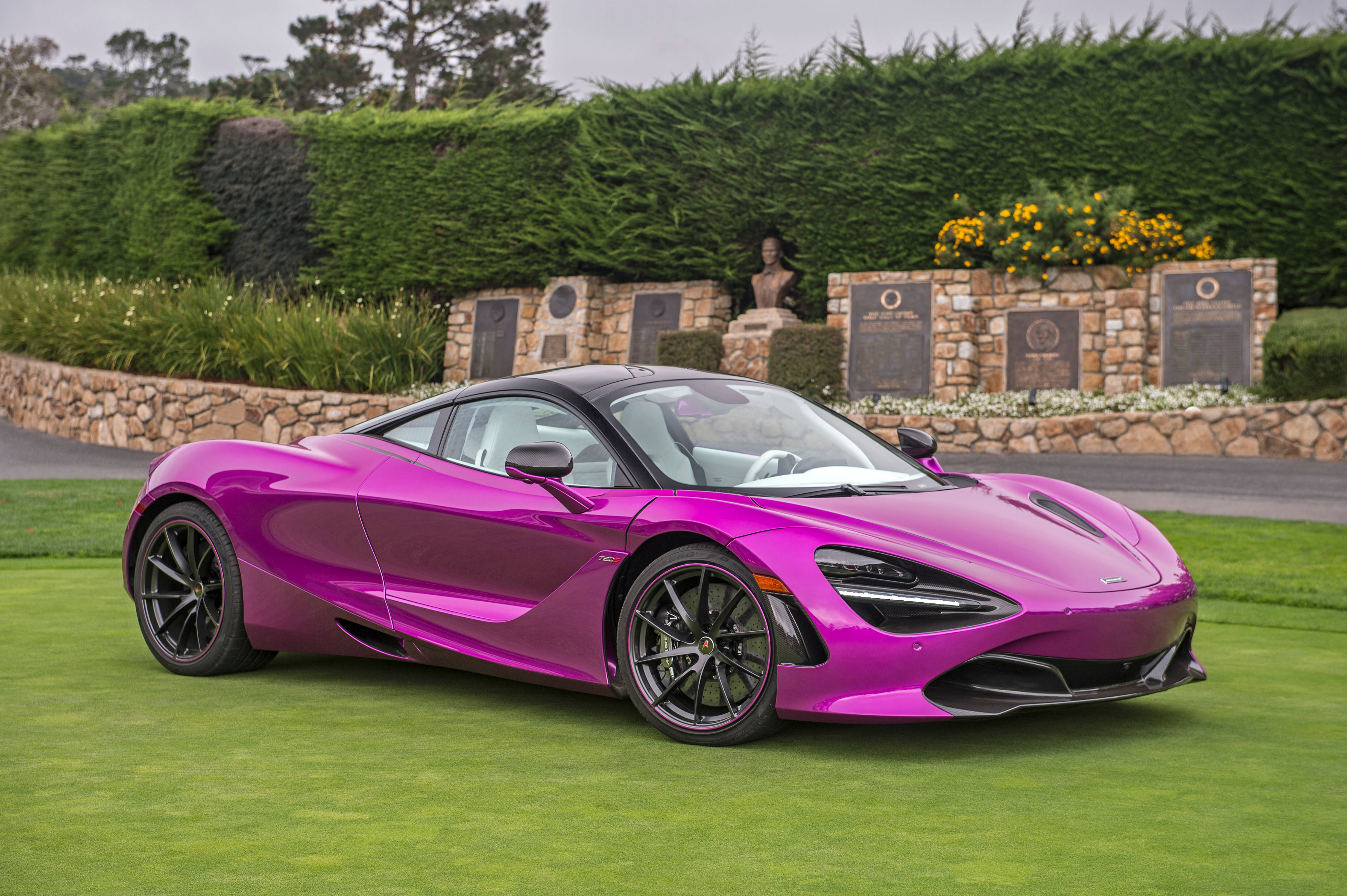 mclaren 720s 4K 桌布 壁紙 — 一輛充滿活力的洋紅色McLaren 720S跑車在修剪整齊的綠色草坪上閃閃發光，旁邊是帶有牌匾和黃色花朵的石牆。
