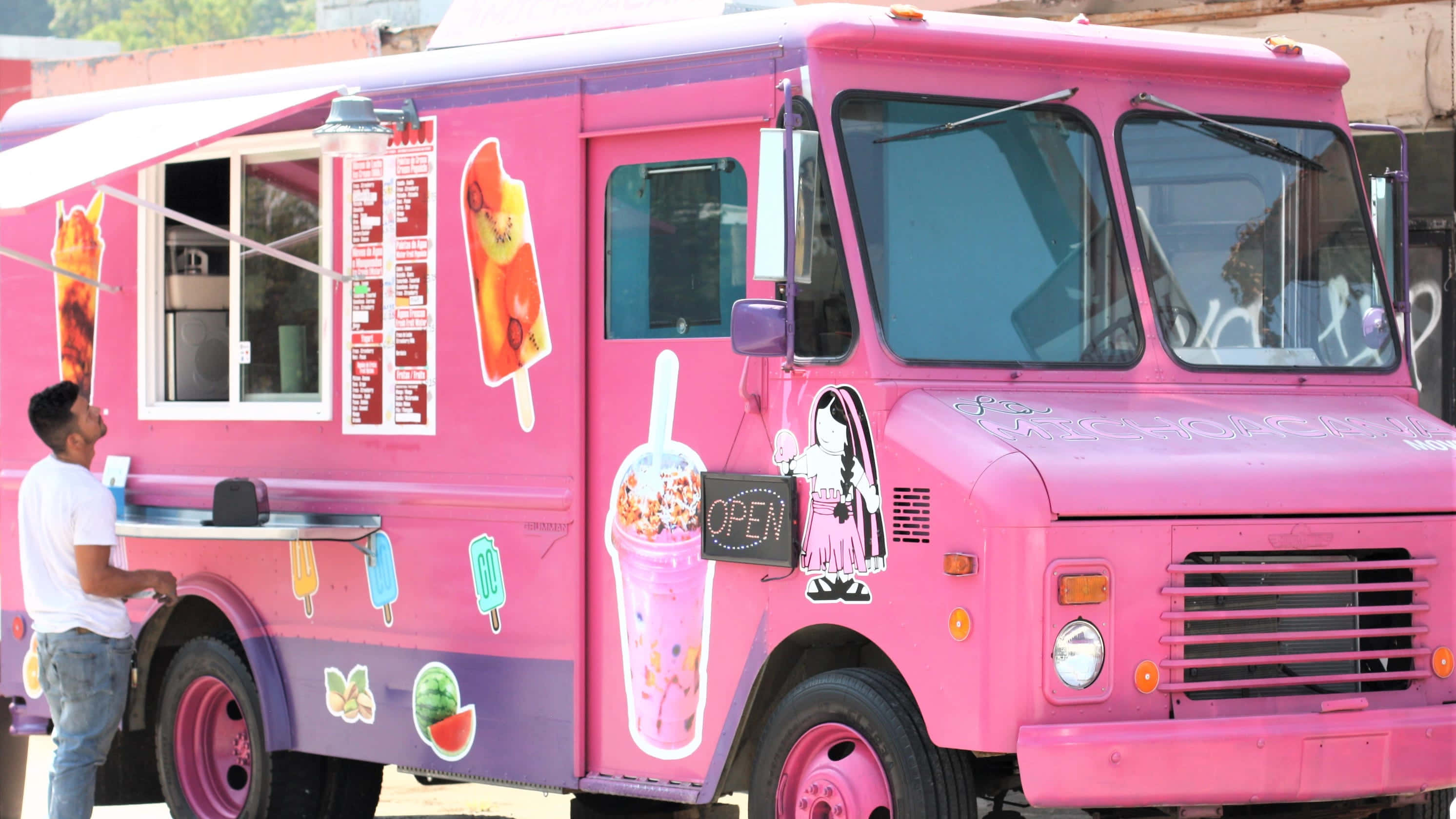 Ice Cream Truck 桌布 壁紙 — 一輛充滿活力的粉紅色冰淇淋車，裝飾著色彩繽紛的甜點圖案，在明亮的日光下為顧客服務。
