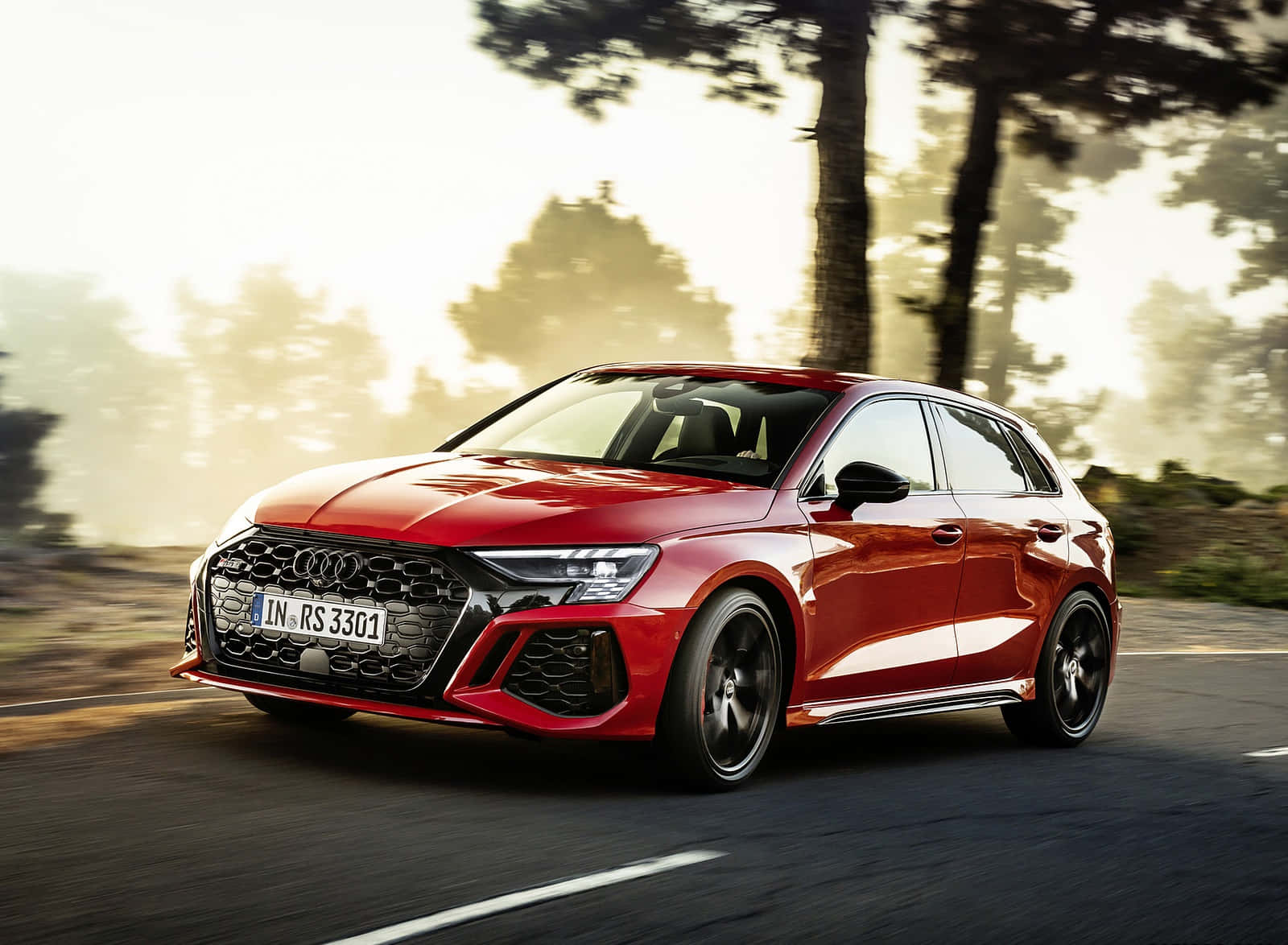 Rs 桌布 壁紙 — 一輛充滿活力的紅色 Audi RS3 Sportback 在沐浴著金色日落光線的林蔭大道上疾馳。