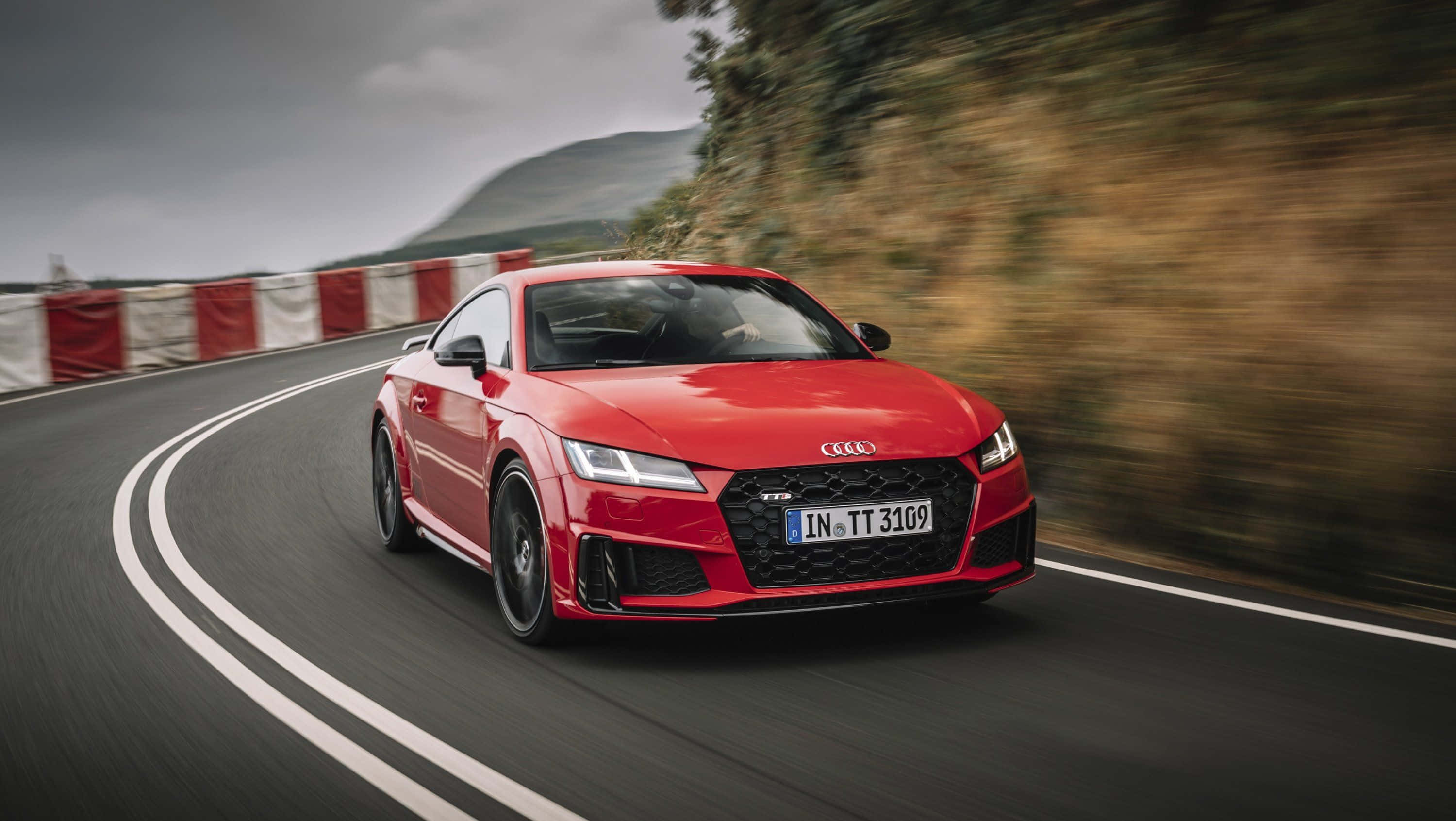 Audi Tt 桌布 壁紙 — 一輛充滿活力的紅色 Audi TT RS 沿著蜿蜒的山路疾馳，帶有動態模糊效果和紅白護欄。