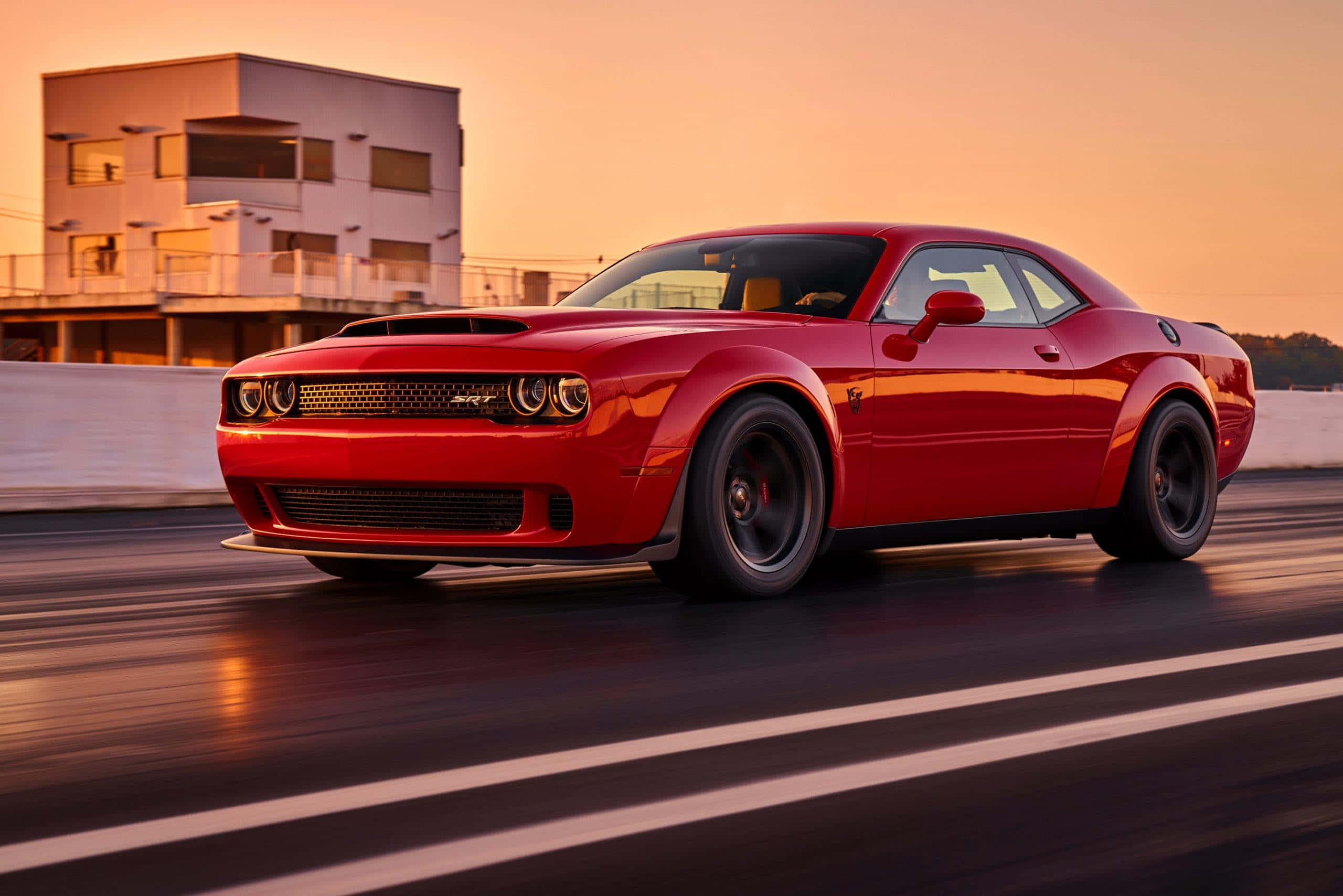 酷車 桌布 壁紙 — 一輛充滿活力的紅色 Dodge Challenger SRT 在日落時分的賽道上奔馳，帶有動態模糊和溫暖的環境光。