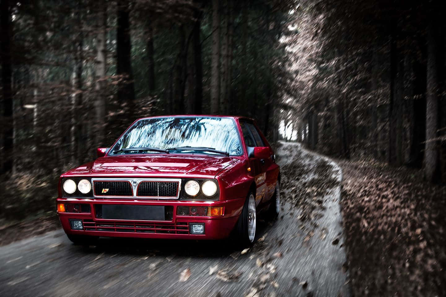 Lancia 桌布 壁紙 — 一輛充滿活力的紅色 Lancia Delta HF Integrale 在森林道路上疾馳，周圍有模糊的動態和旋轉的秋葉。