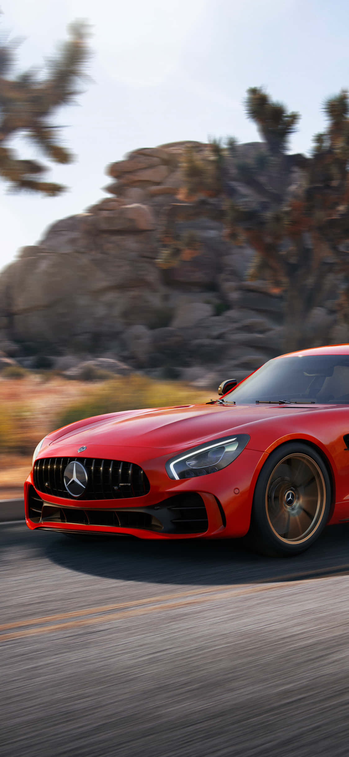 iPhone X Amg Gt-r 桌布 壁紙 — 一輛充滿活力的紅色 Mercedes-AMG GT 在沙漠公路上疾馳，背景是模糊的岩石 formations 和約書亞樹。