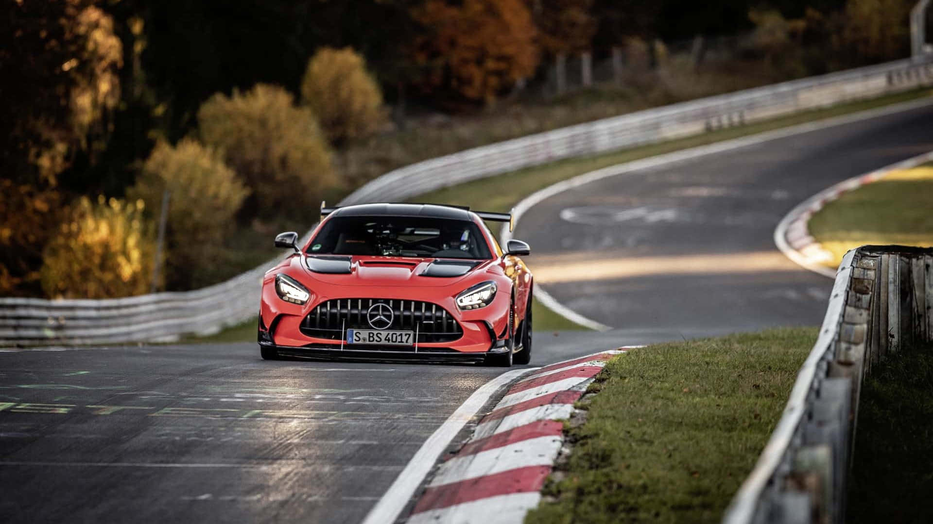 Mercedes Gts 桌布 壁紙 — 一輛充滿活力的紅色 Mercedes-AMG GT R 賽車沿著蜿蜒的瀝青賽道疾馳，賽道兩旁是秋葉和紅白相間的賽道邊緣。