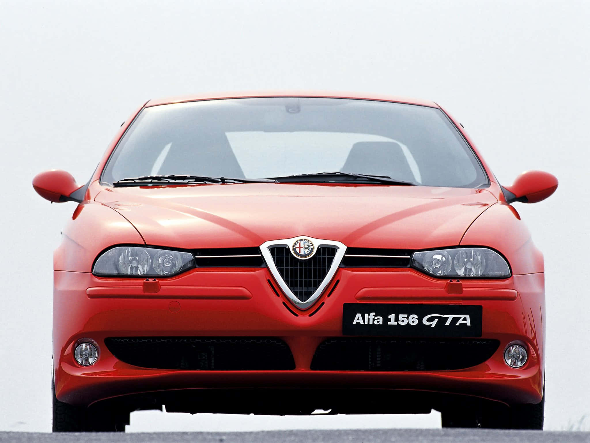 Alfa Romeo 156 桌布 壁紙 — 一輛充滿活力的紅色Alfa 156 GTA跑車正面朝向純白色背景，展示其標誌性格柵和時尚車頭燈。