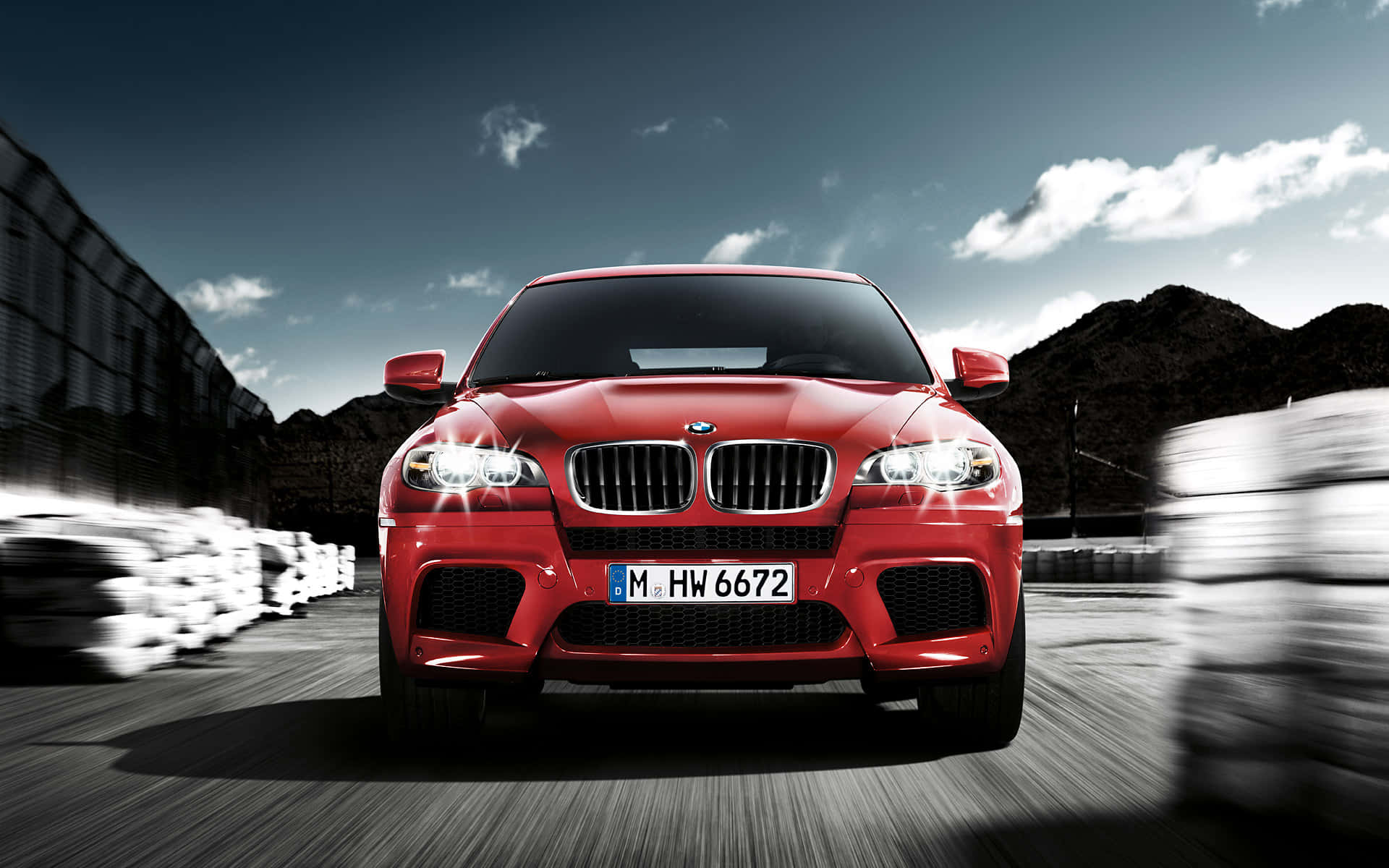 BMW X6 M 桌布 壁紙 — 一輛充滿活力的紅色BMW M1跑車在賽道上疾馳，帶有動態模糊和戲劇性的天空。