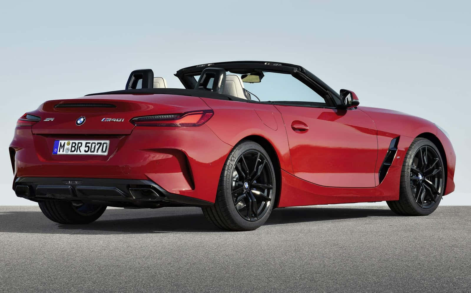 Bmw Z4 桌布 壁紙 — 一輛充滿活力的紅色BMW Z4敞篷跑車，帶有黑色飾件和流線型設計，停泊在晴朗天空下的瀝青路面上。