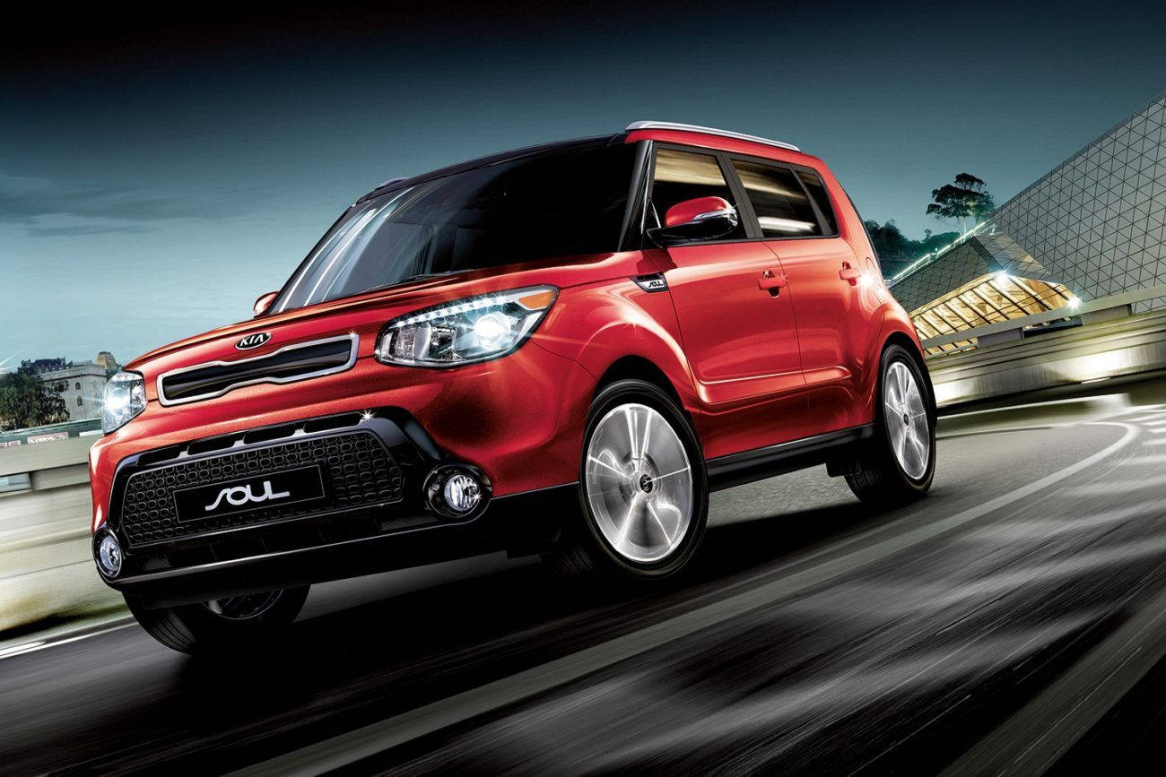 Kia 桌布 壁紙 — 一輛充滿活力的紅色Kia Soul在暮色中沿著模糊的城市高速公路奔馳，背景是現代建築。