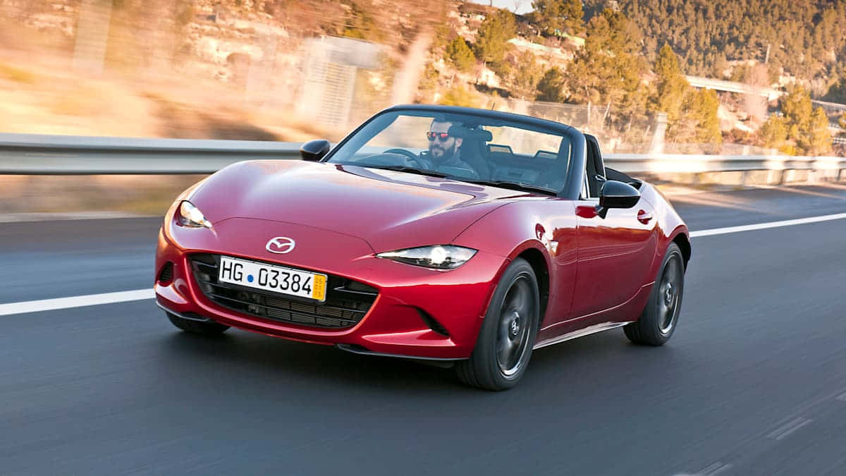 Fiat 124 Spider 桌布 壁紙 — 一輛充滿活力的紅色Mazda MX-5 Miata敞篷跑車在蜿蜒的山路上奔馳，背景模糊。