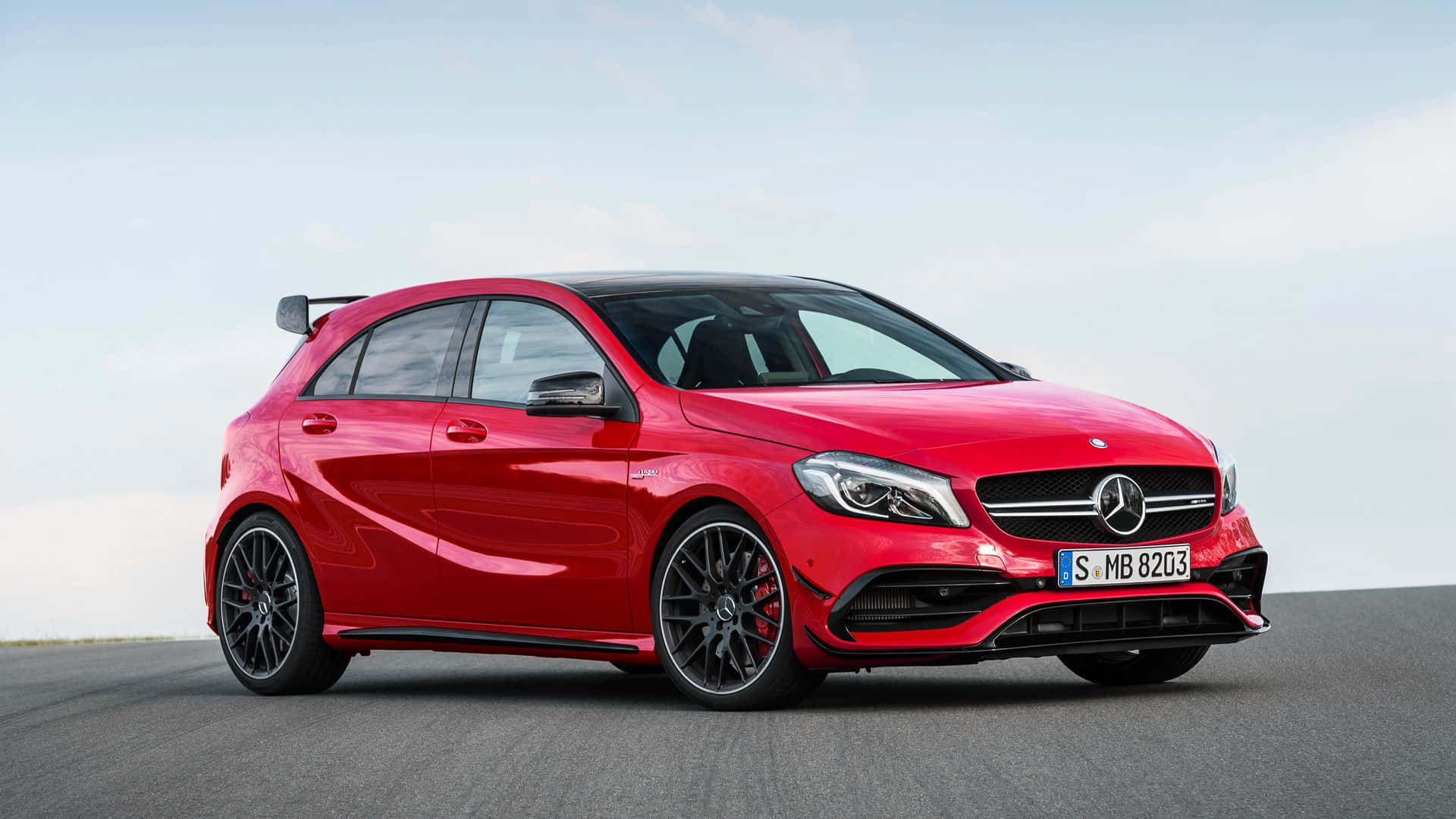 桌布 壁紙 — 一輛充滿活力的紅色Mercedes-AMG A45 S跑車，帶有黑色飾件和後尾翼，停在開闊的瀝青路面上，天空晴朗。