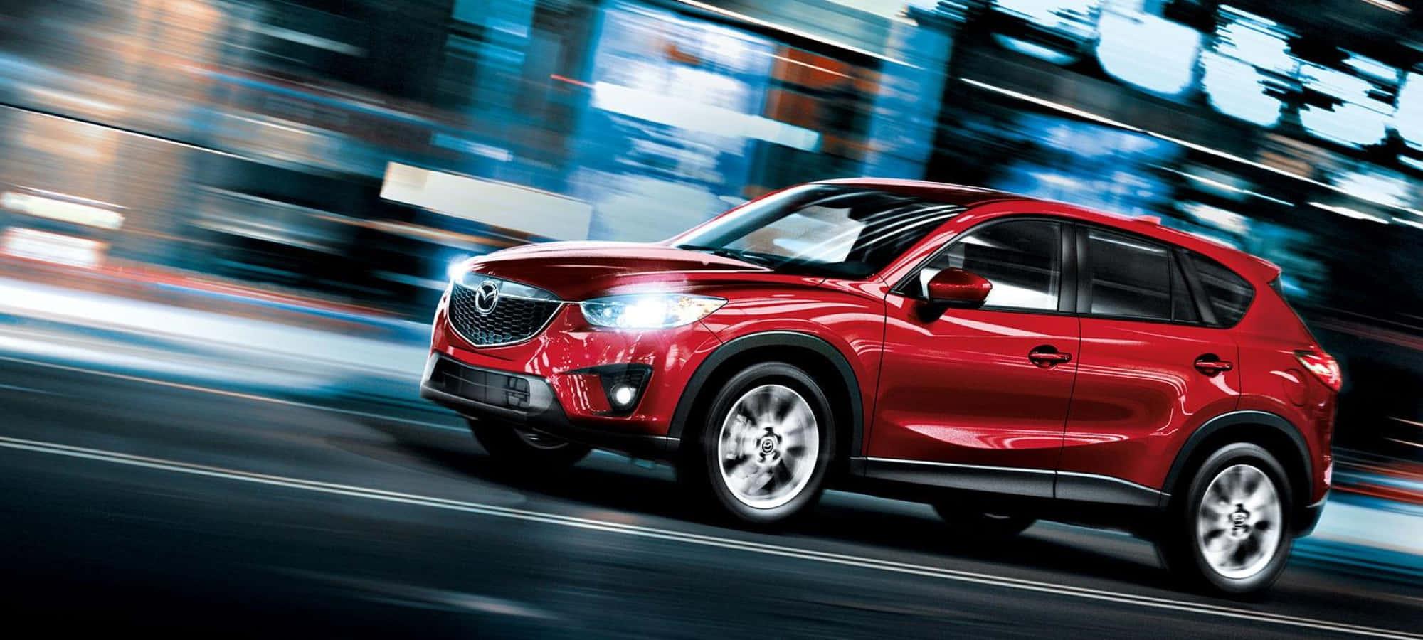 Mazda Cx-30 桌布 壁紙 — 一輛充滿活力的紅色SUV在夜晚穿過模糊的城市景觀，帶有流光溢彩的光線。