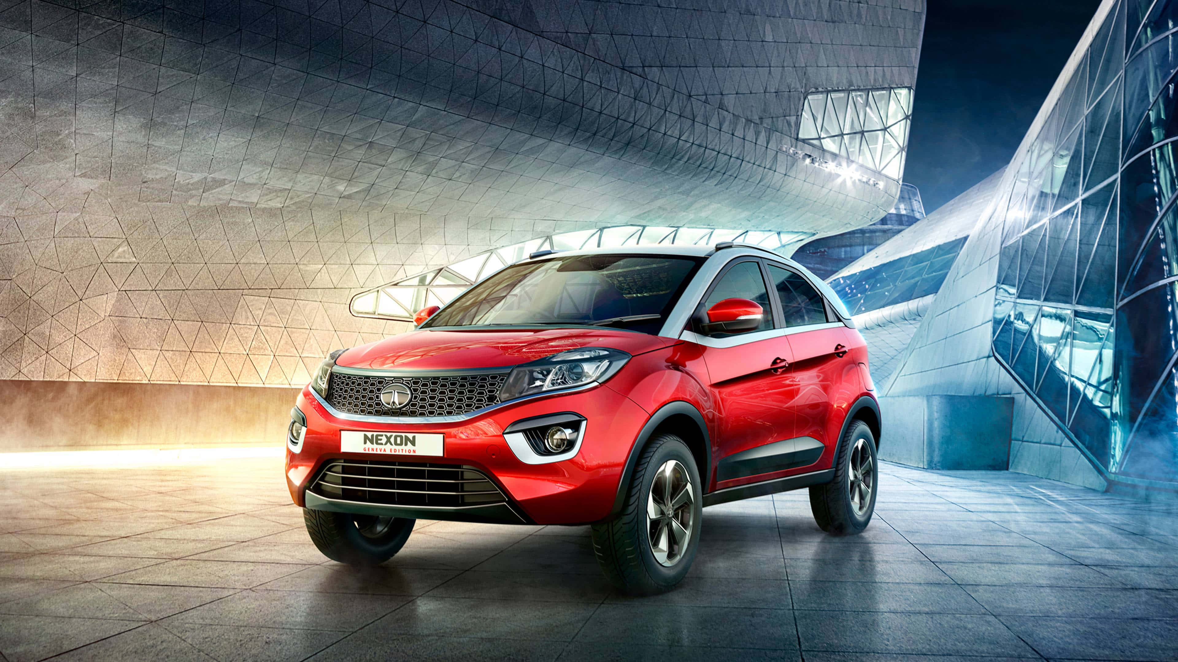 Tata Motors 桌布 壁紙 — 一輛充滿活力的紅色SUV在戲劇性的燈光下，以未來風格的玻璃和鋼鐵建築為背景閃閃發光。