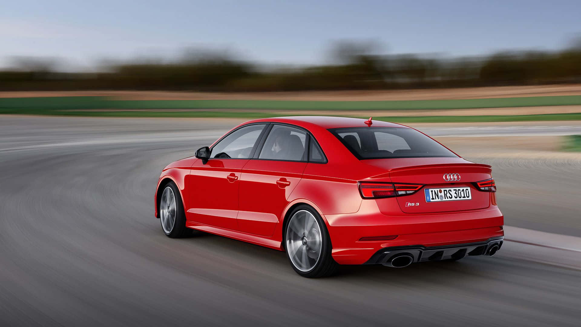 Audi Rs3 桌布 壁紙 — 一輛充滿活力的紅色奧迪RS3轎車在賽道上高速行駛，動態模糊傳達出高速和力量。