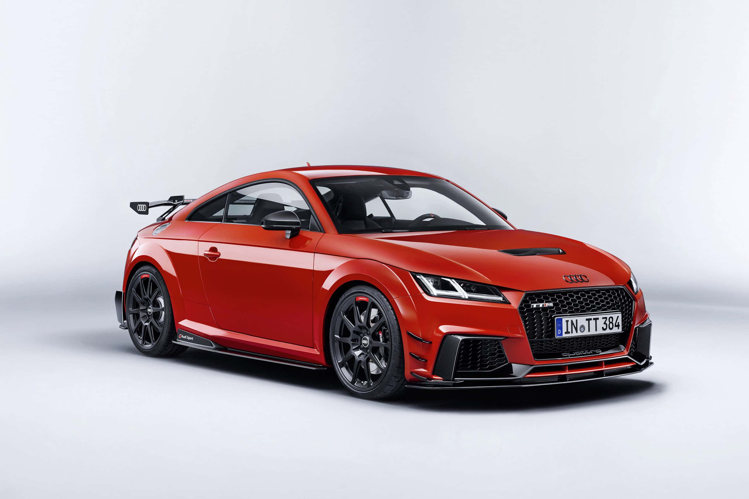 Audi Tt Rs 桌布 壁紙 — 一輛充滿活力的紅色奧迪TT RS跑車，帶有黑色飾件和後擾流板，置於潔淨的白色工作室背景前。