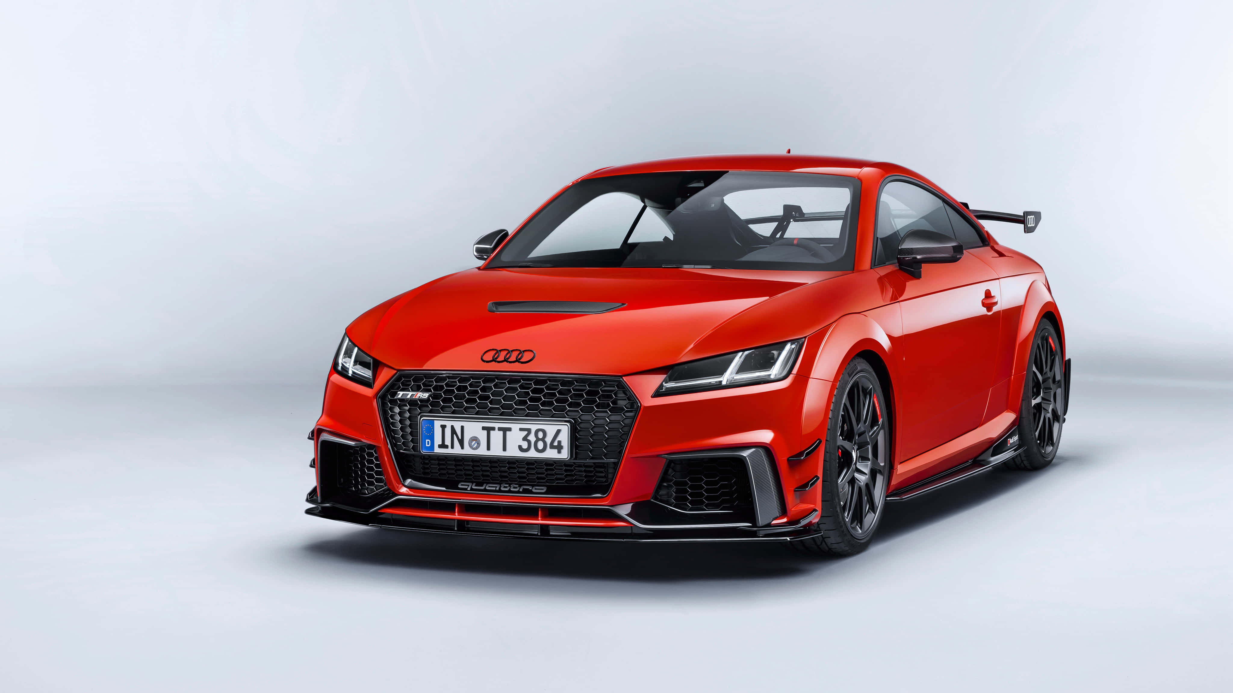 Audi Tt Rs 桌布 壁紙 — 一輛充滿活力的紅色奧迪TT RS跑車，帶有黑色飾件和後擾流板，在極簡的淺灰色工作室背景前擺拍。
