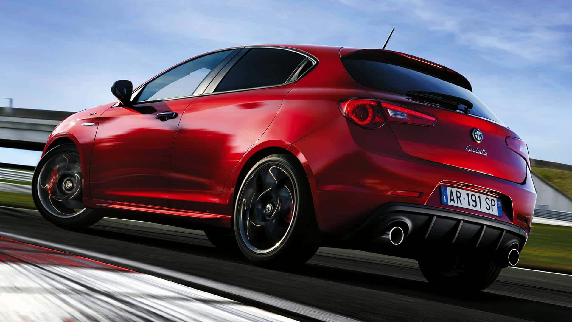 Alfa Romeo Giulietta 桌布 壁紙 — 一輛充滿活力的紅色愛快羅密歐Giulietta在晴朗藍天下沿著賽道疾馳，帶有動態模糊效果。