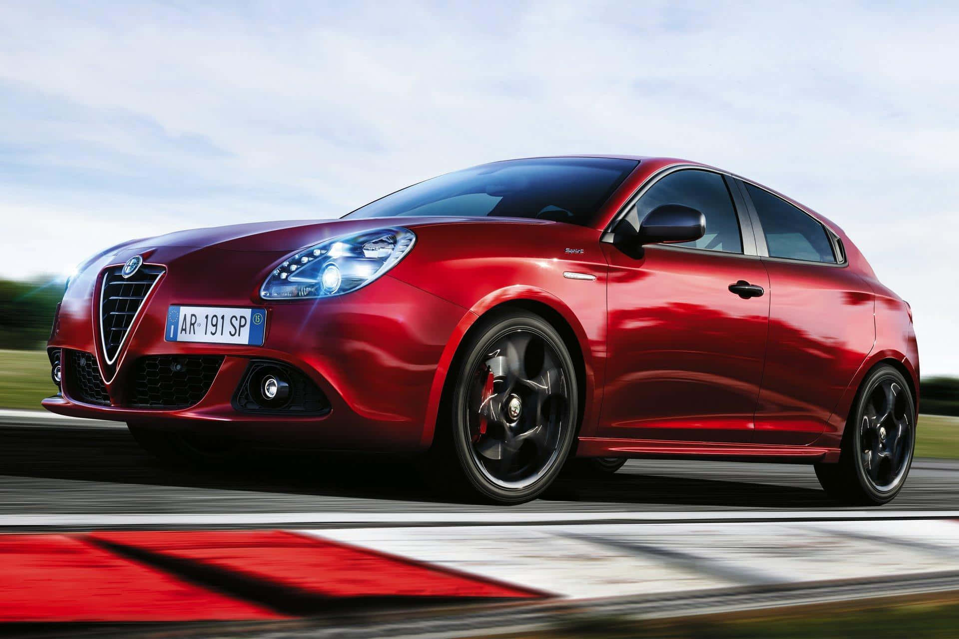 Alfa Romeo Giulietta 桌布 壁紙 — 一輛充滿活力的紅色愛快羅密歐Giulietta跑車在賽道上疾馳，帶有動態模糊效果和動感天空背景。